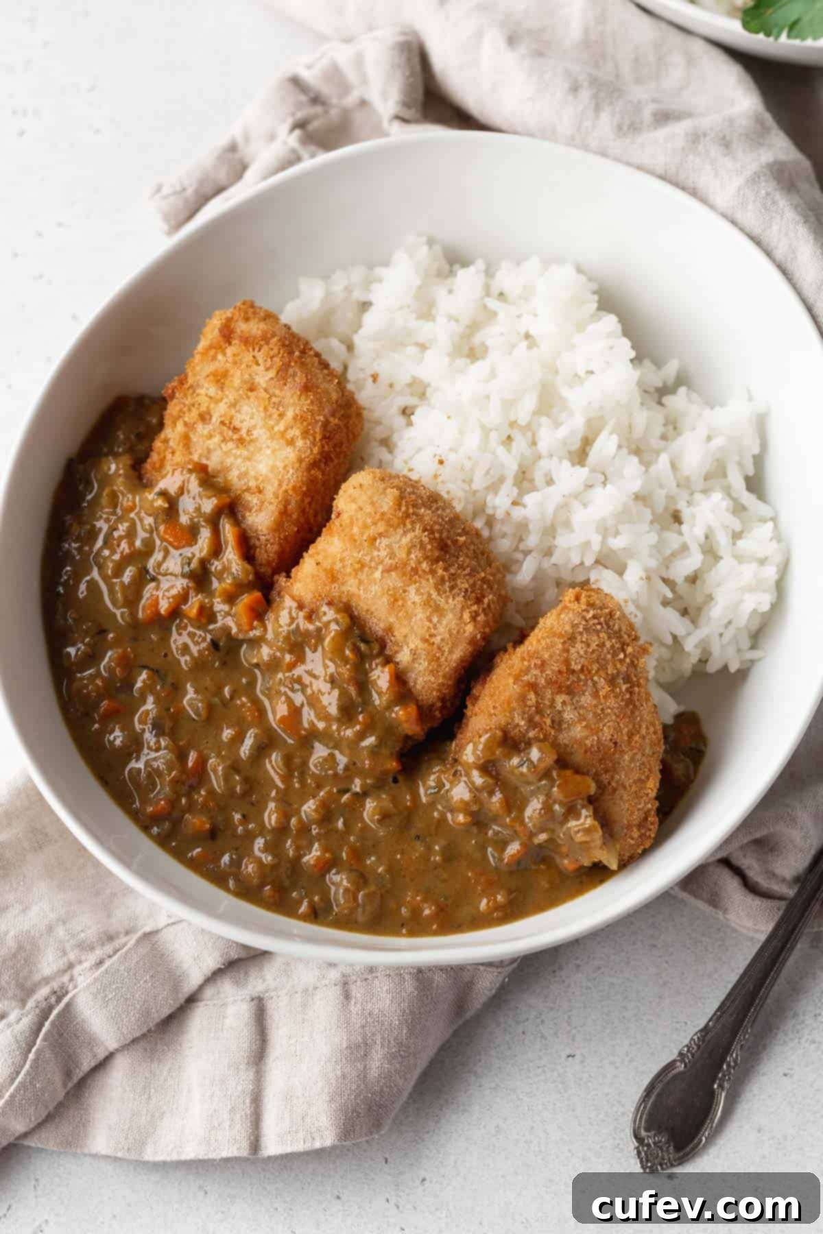 A perfectly portioned bowl of fluffy white rice crowned with golden-brown katsu slices, generously covered in a rich and flavorful vegan curry sauce.