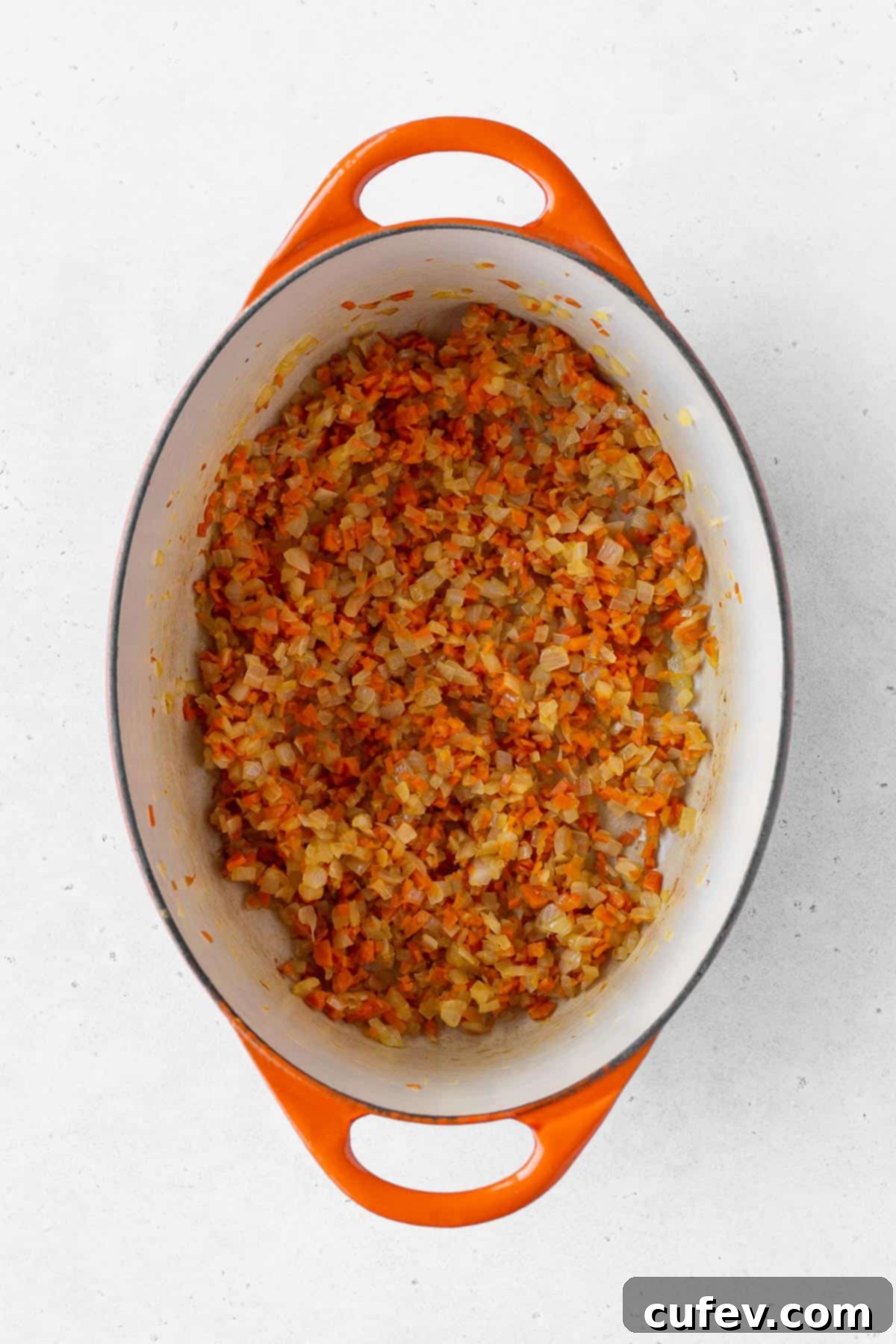 Finely minced onion and carrots gently cooking in an enameled pot, beginning to caramelize and release their natural sweetness.