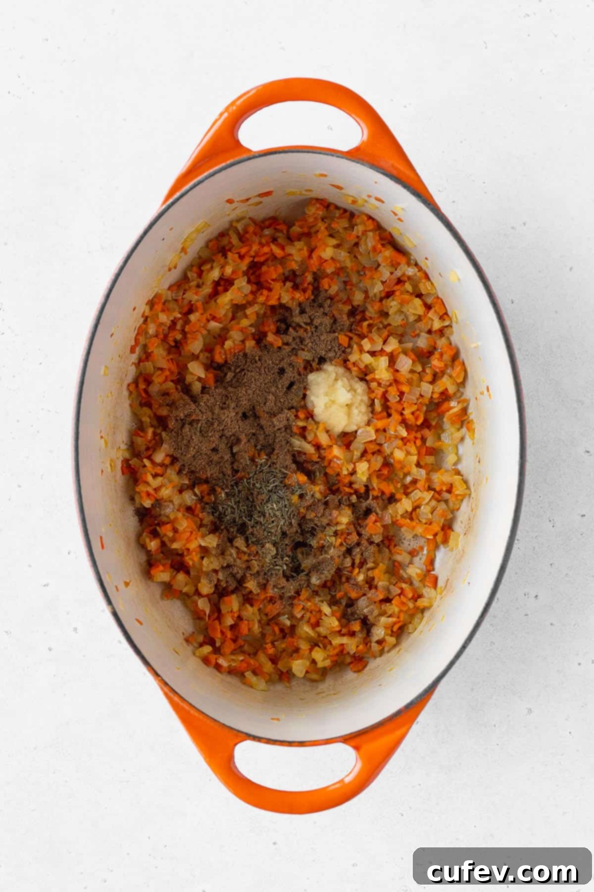 Close-up of garam masala, dried thyme, and freshly grated garlic added to the sautéed vegetables in the pot, infusing the base with rich aromatics.