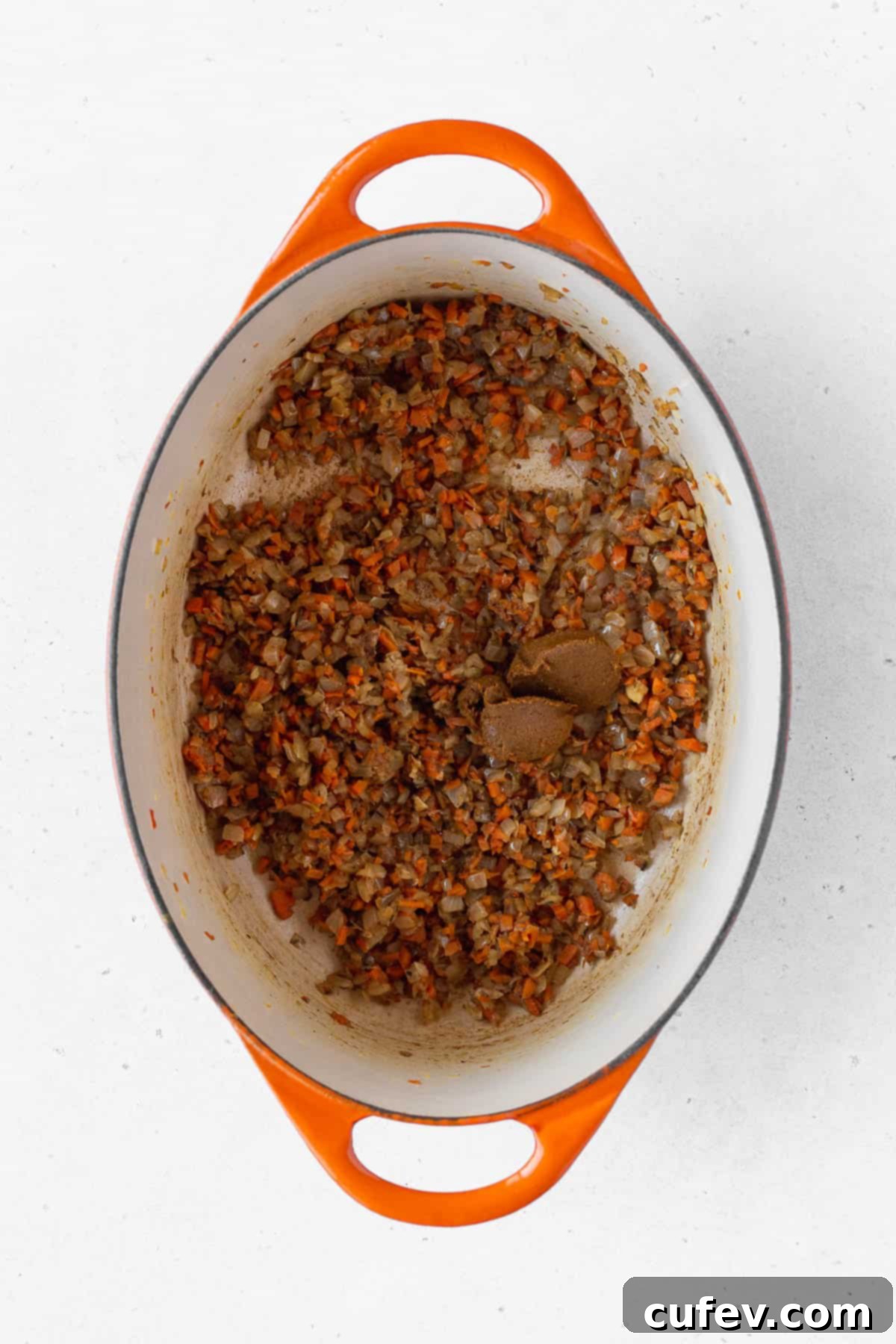 Rich yellow curry paste being incorporated into the sautéed onion and carrot mixture, creating a fragrant and flavorful base for the sauce.