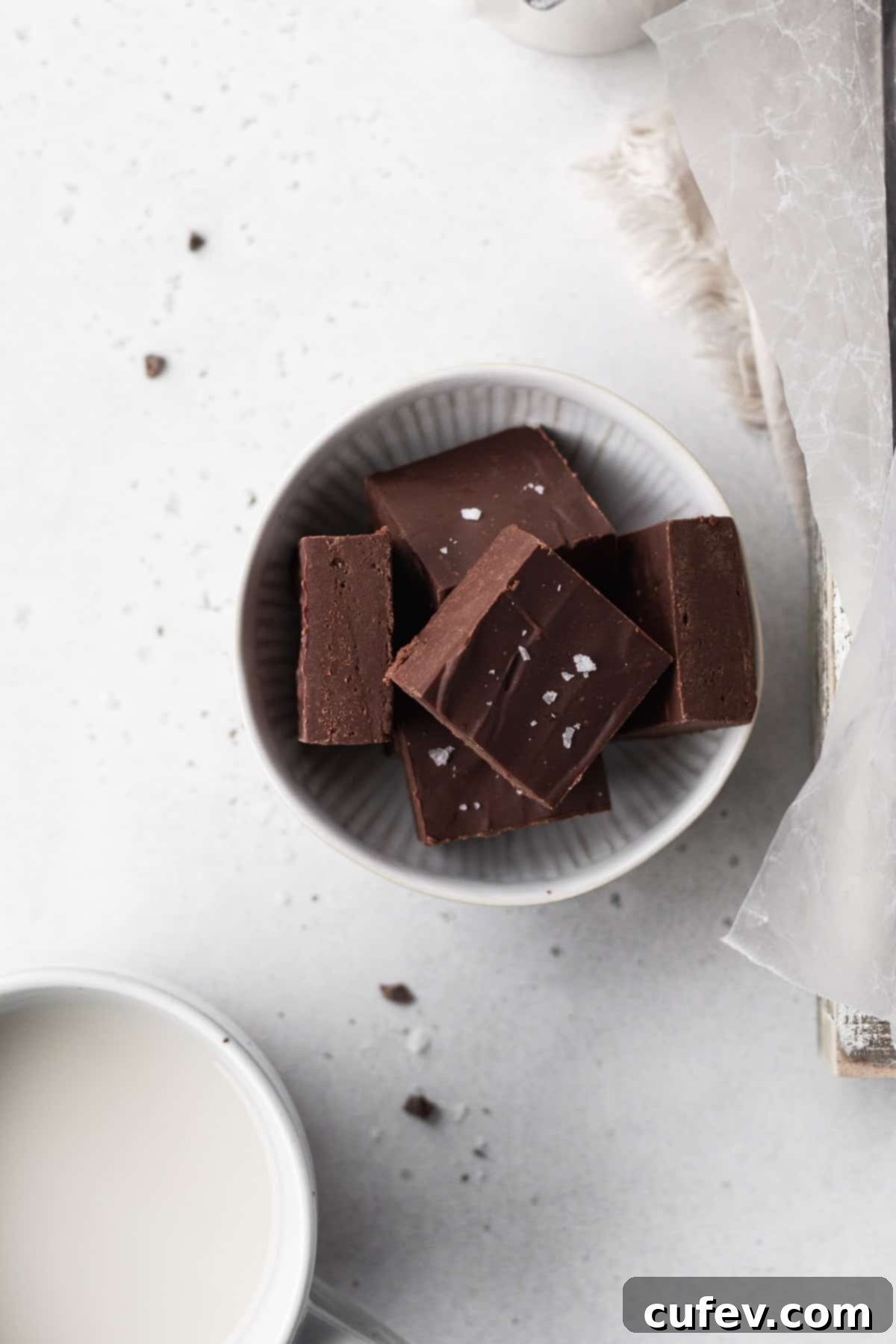 Overhead shot of cubes of dairy-free fudge in a white bowl on a white table.