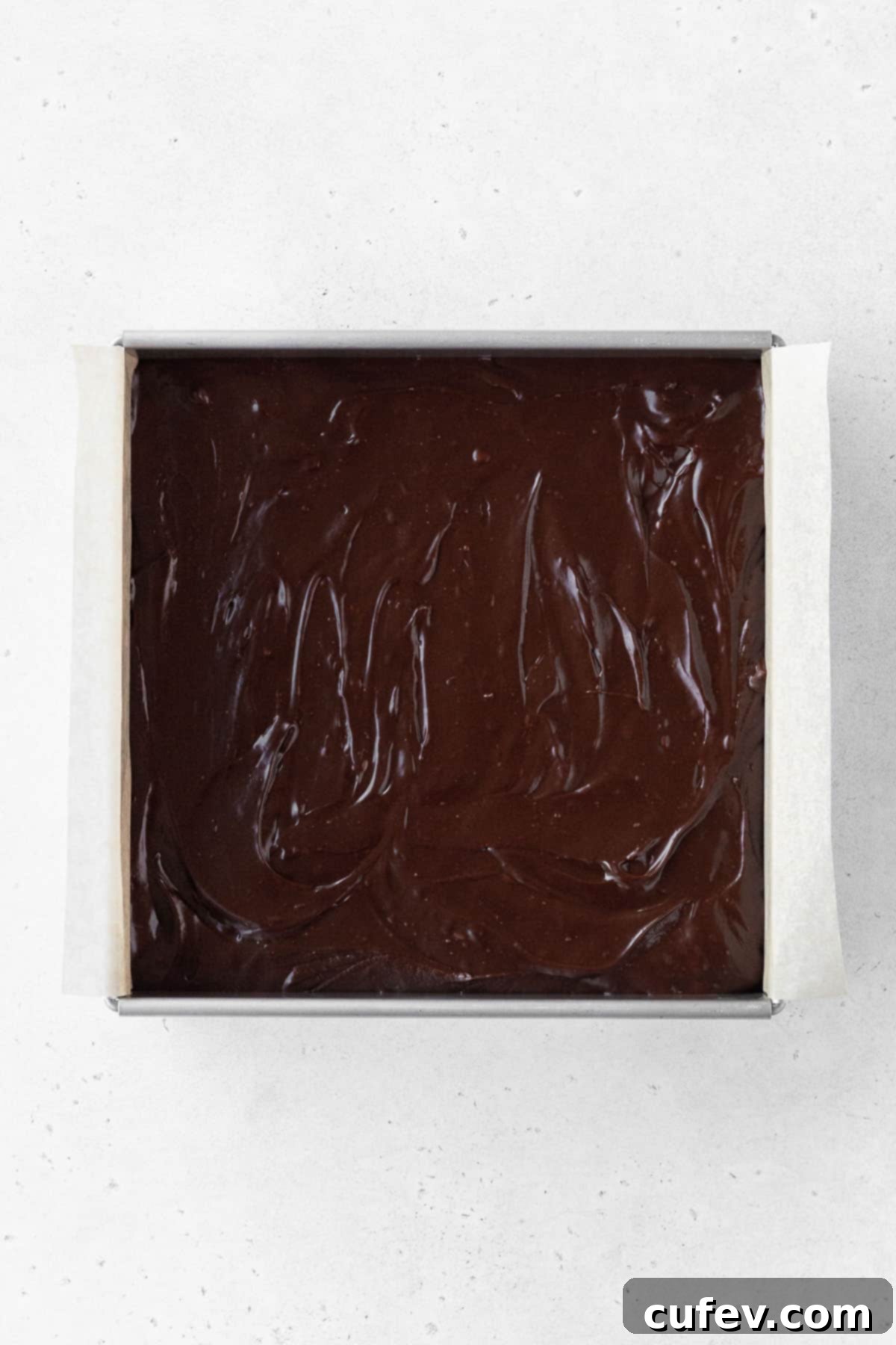 Dairy-free fudge batter poured into the parchment-lined baking tin and smoothed out with a spatula.