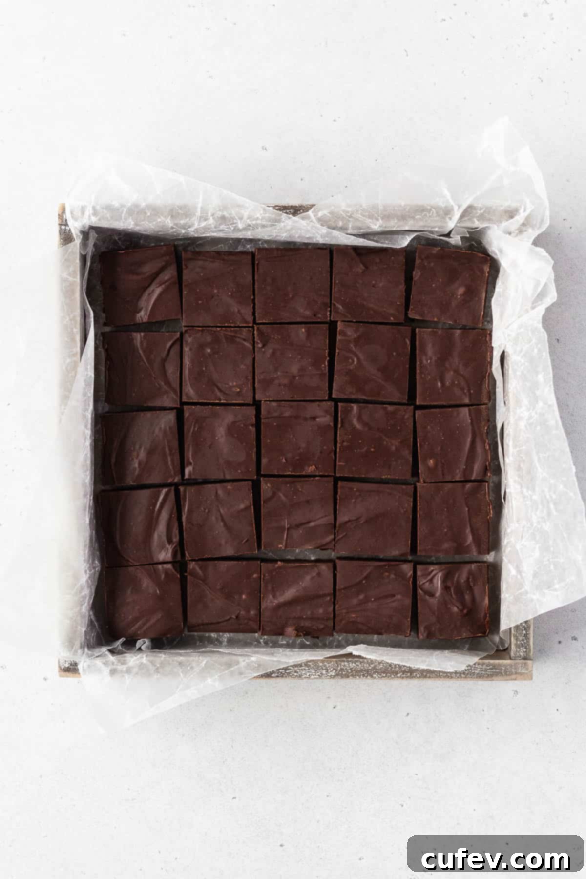 Finished batch of dairy-free vegan fudge in a wooden box with parchment paper after being cut into squares.