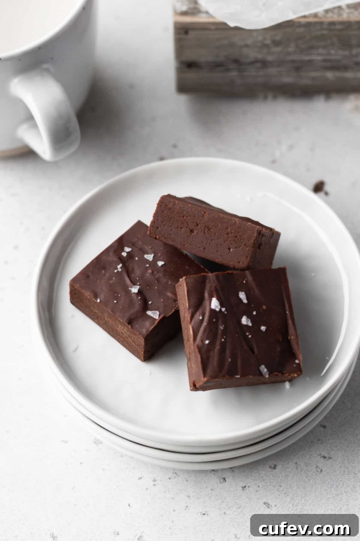 3 squares of dairy free fudge on a white plate with a mug of plant-based milk to the side.