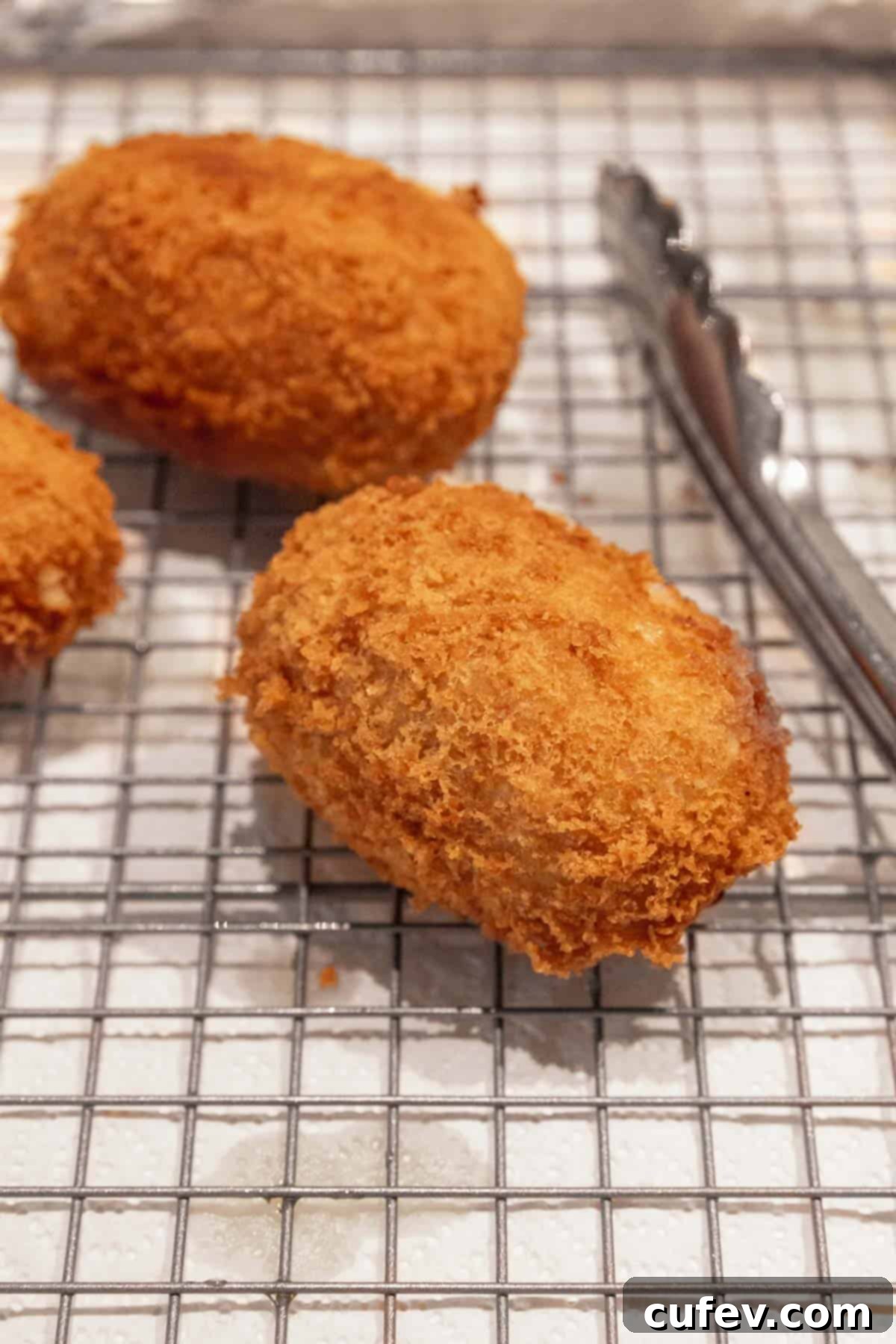 Close up shot of a golden, crispy potato croquette draining on a wire rack above paper towels.