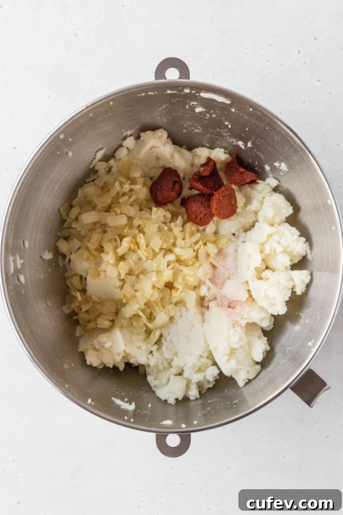 Sautéed onion mix and curry paste added to bowl with mashed potato mix.