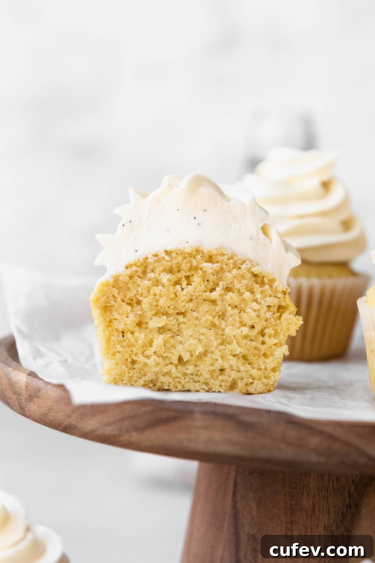 Guilt-Free Cupcakes 11 A dairy free vanilla cupcake with creamy dairy-free vanilla buttercream, placed on a wooden stand and cut in half to showcase its fluffy and tender interior crumb.