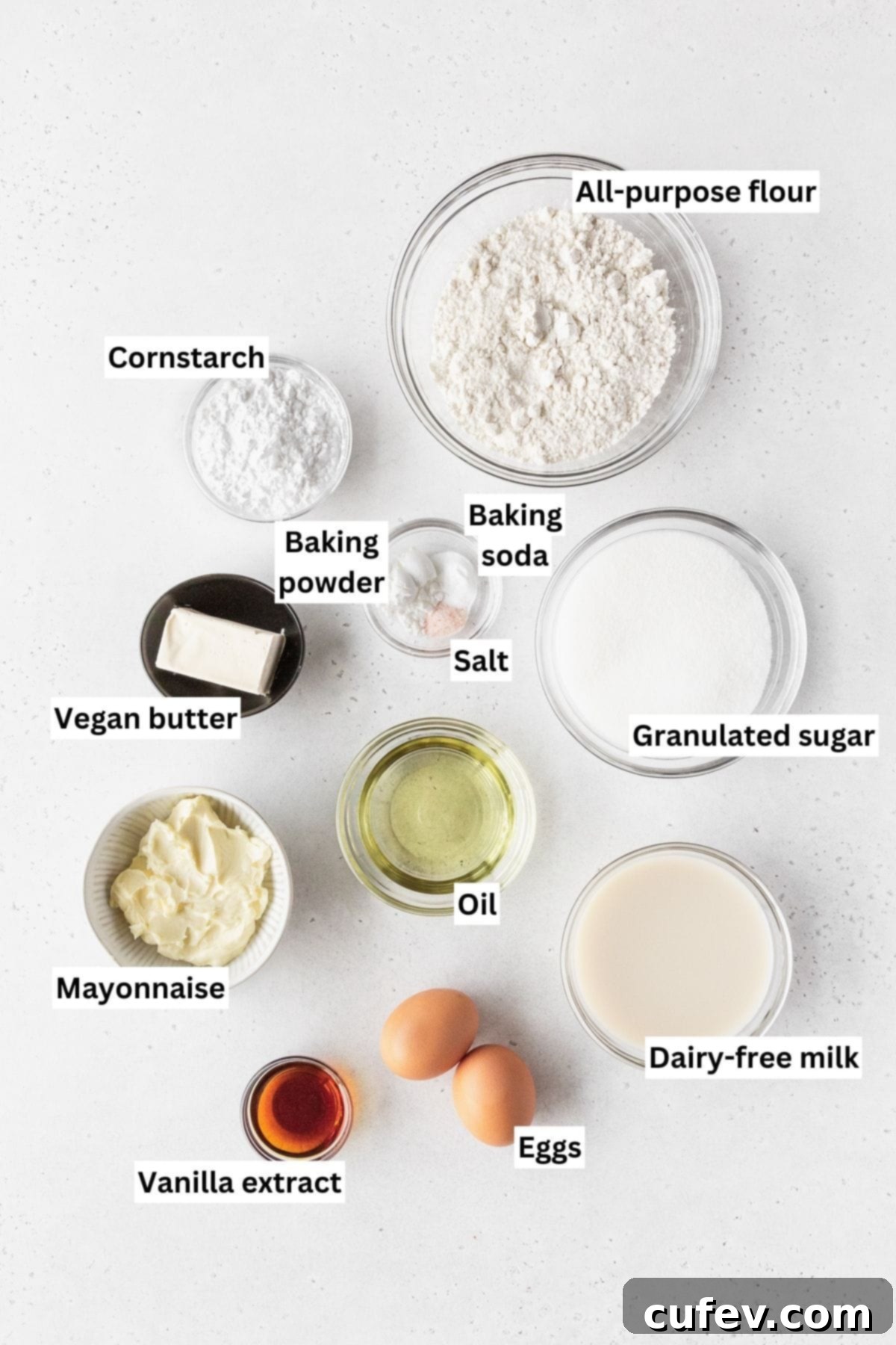 Guilt-Free Cupcakes 3 Ingredients for making dairy-free vanilla cupcakes laid out neatly on a white table, including flour, sugar, vegan butter, eggs, vanilla, and plant-based milk.