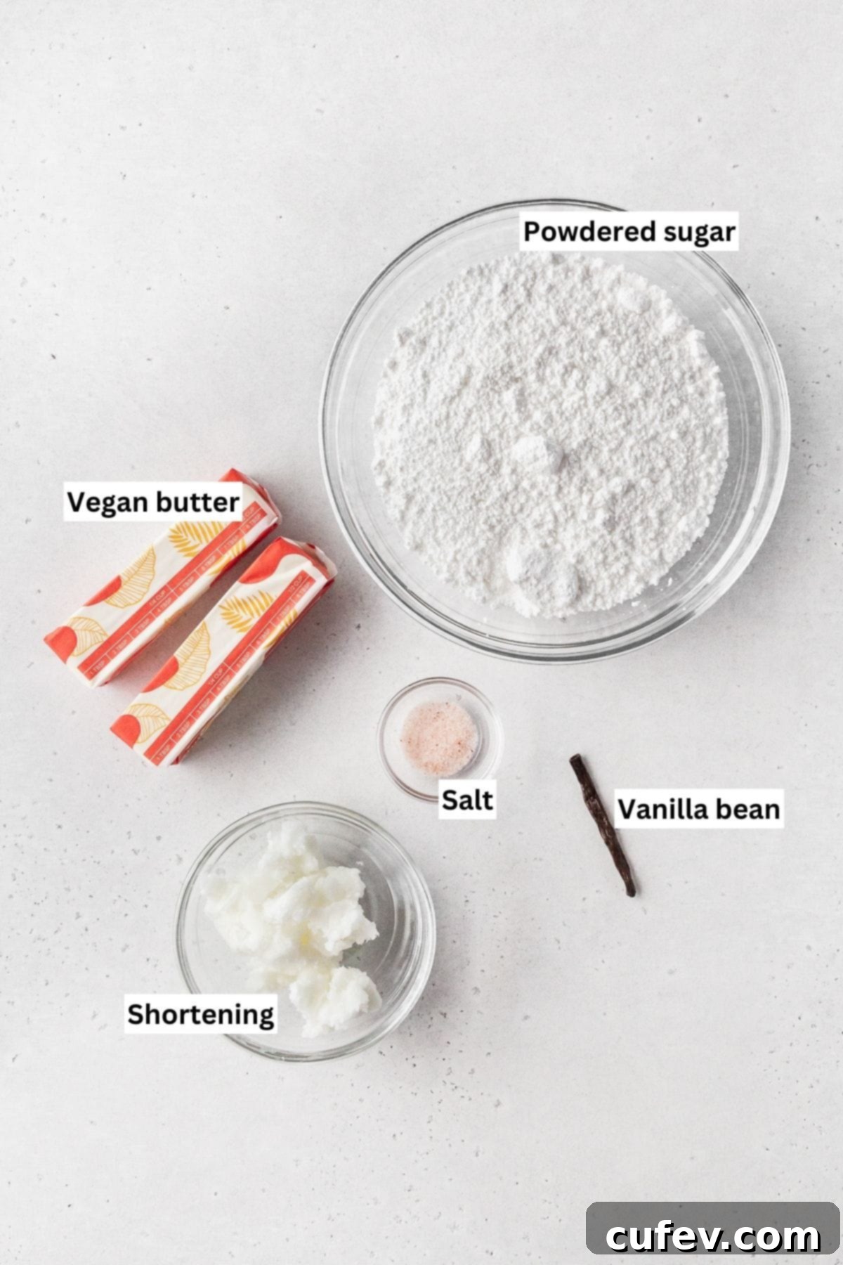Guilt-Free Cupcakes 4 Ingredients for making vegan vanilla buttercream frosting laid out on a white table, including vegan butter, shortening, powdered sugar, and a vanilla bean.
