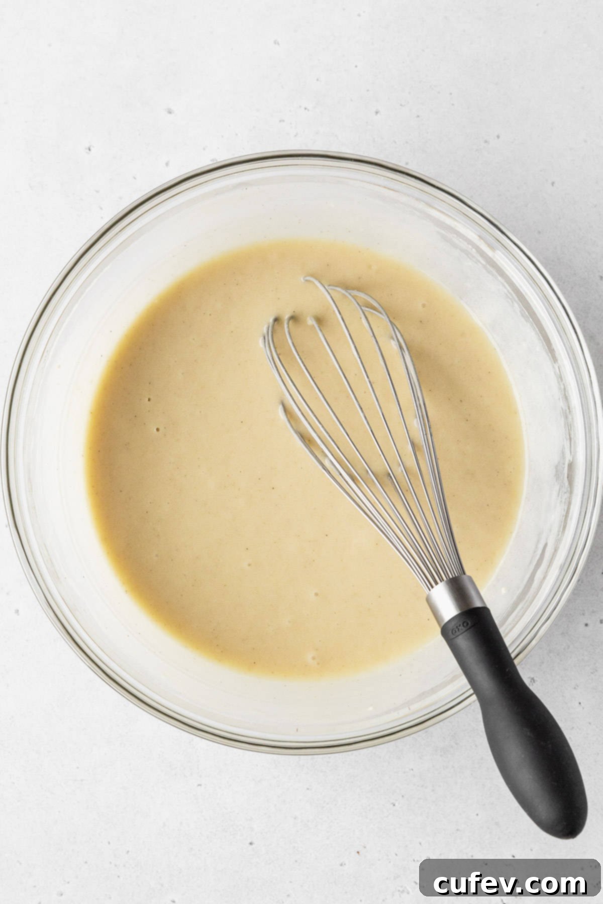 Guilt-Free Cupcakes 7 Completed dairy-free vanilla cupcake batter in a clear mixing bowl, smooth and ready to bake, with a black-handled whisk resting beside it.