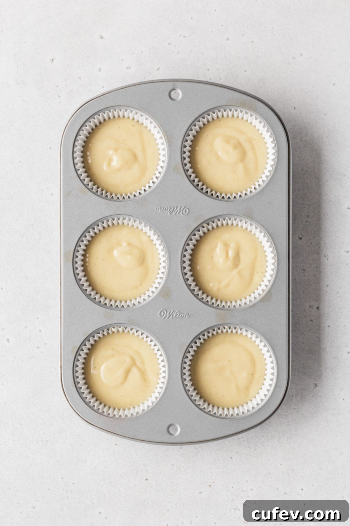 Guilt-Free Cupcakes 8 Muffin tin with white paper liners filled evenly with dairy-free vanilla cupcake batter, before being placed in the oven.