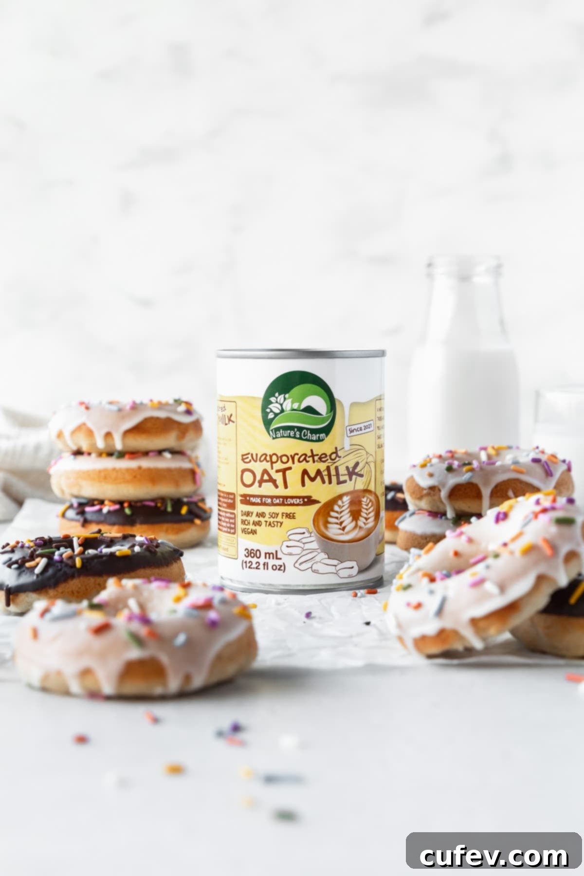 Can of Nature's Charm evaporated oat milk in the center of a table with vegan dairy-free donuts all around.