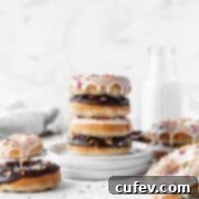Stack of alternating chocolate and vanilla glazed baked vegan donuts on a stack of white dessert plates with a jug of non-dairy milk in the background.