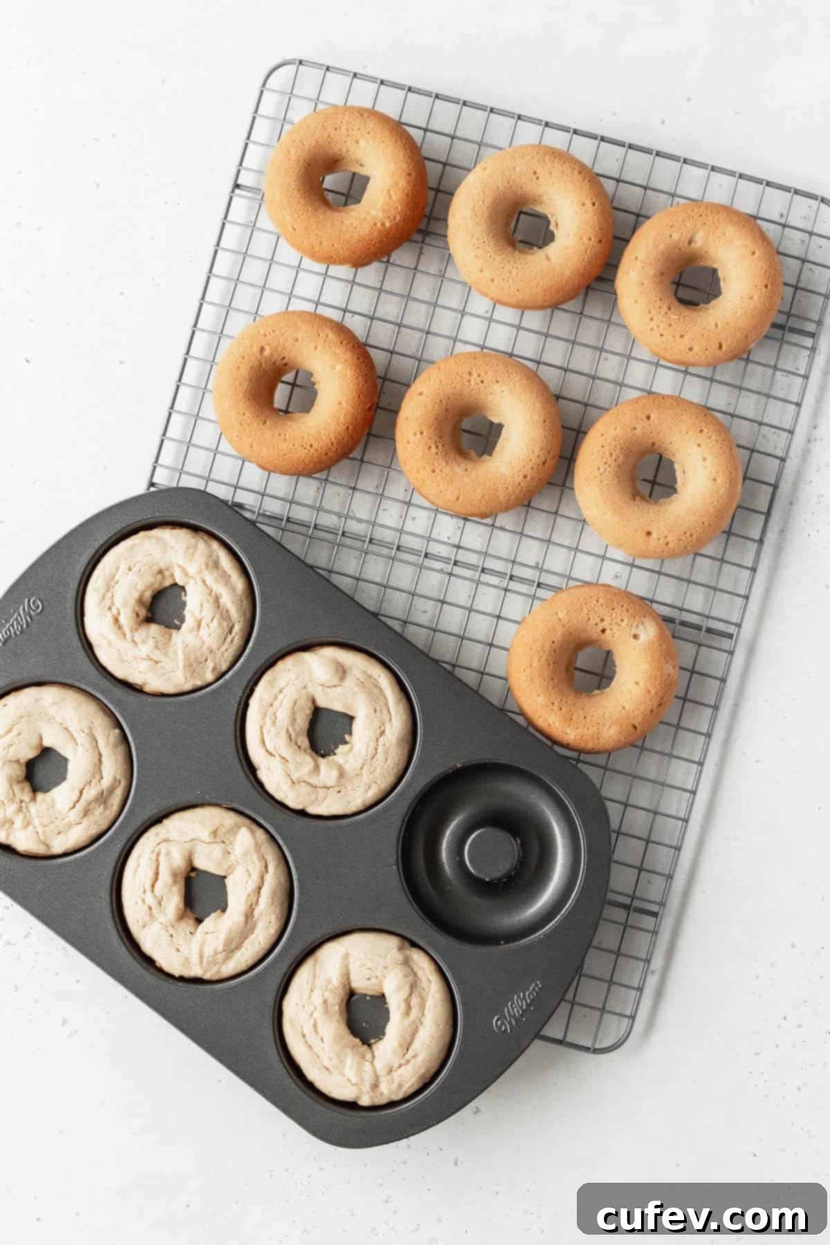 Overhead shot of a pan of gluten free dairy free doughnuts on a wire rack with more donuts that have been removed the pan are cooling.