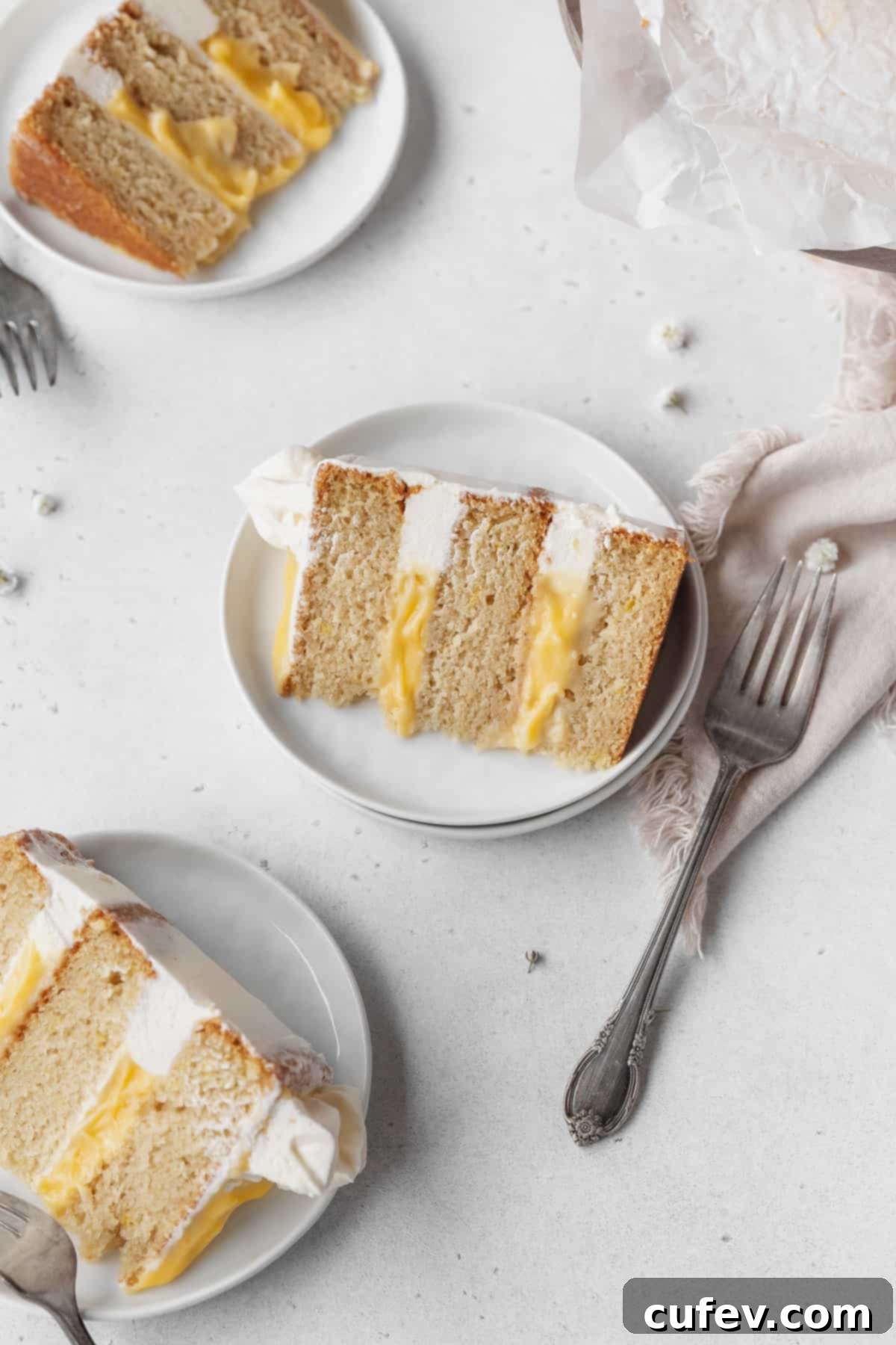 Overhead shot of 3 slices of dairy-free lemon curd layer cake on white dessert plates with silver forks.