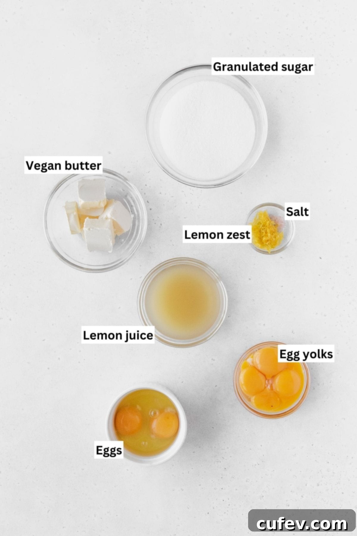 Lemon curd ingredients measured out into small glass bowls on a white table with text overlay.