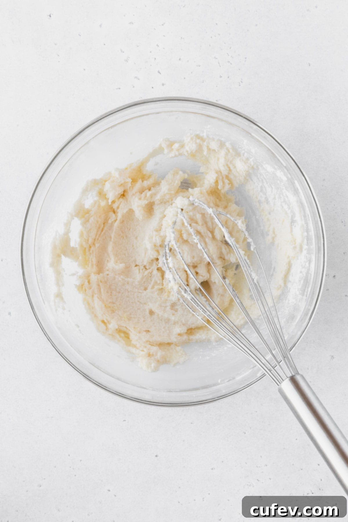 Mixing together the sugar, salt, lemon zest, and eggs in a glass bowl with a silver whisk.