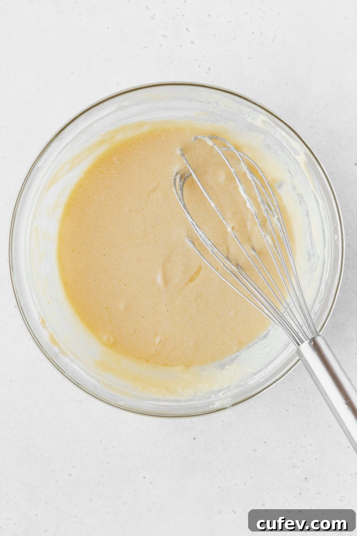 Lemon curd ingredients mixed together in a glass bowl with a whisk.