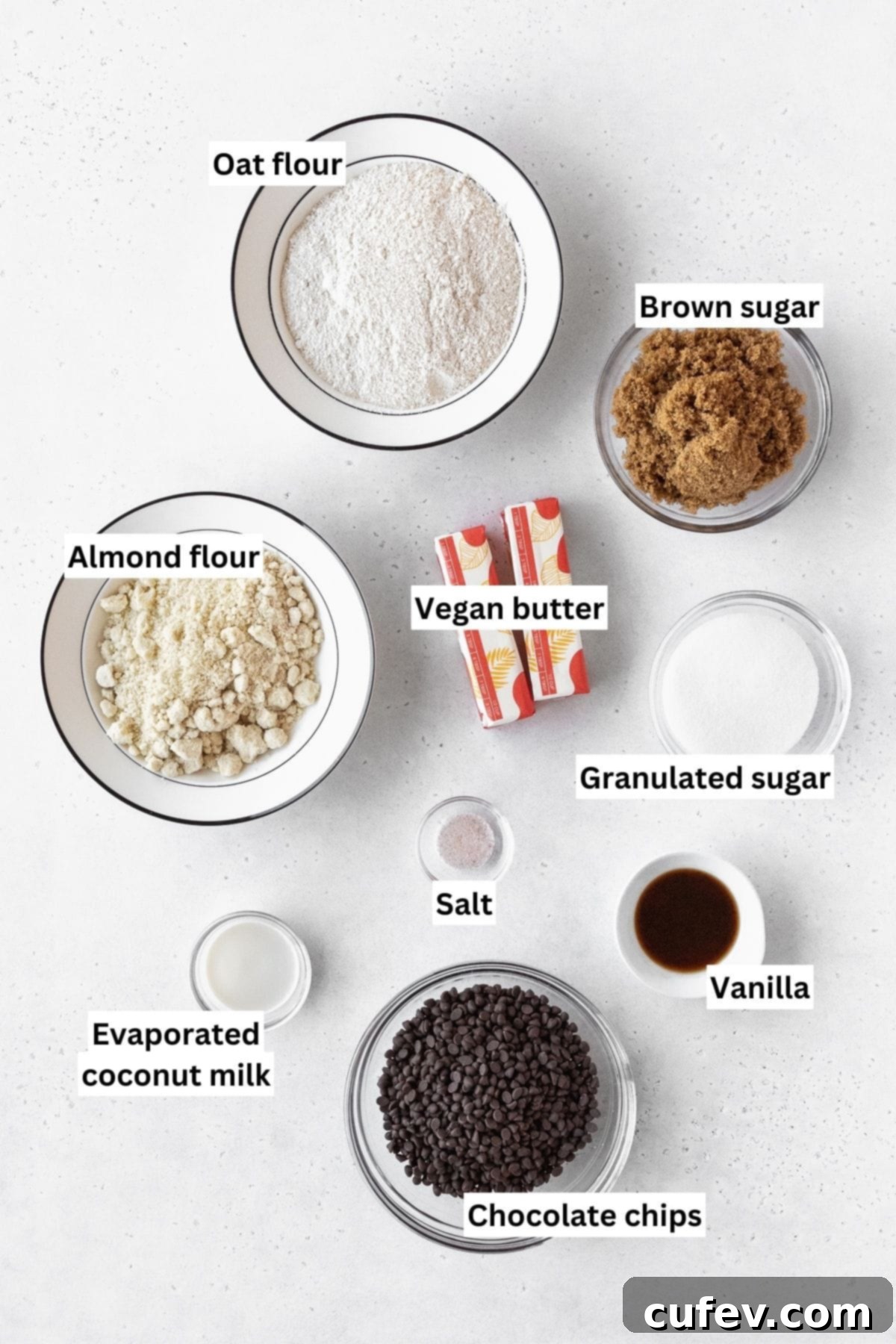 All ingredients needed to make gluten-free edible sugar cookie dough are measured out neatly in small bowls on a white table.