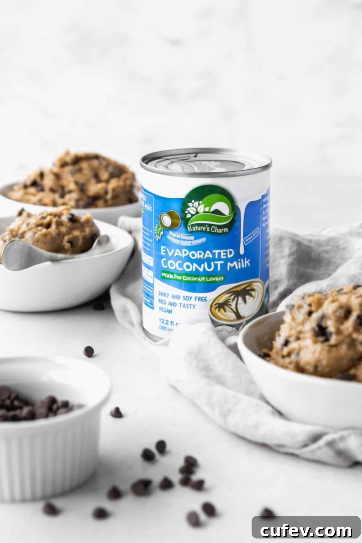 Can of Nature's Charm evaporated coconut milk placed in the center of an array of bowls, some filled with vegan edible cookie dough.