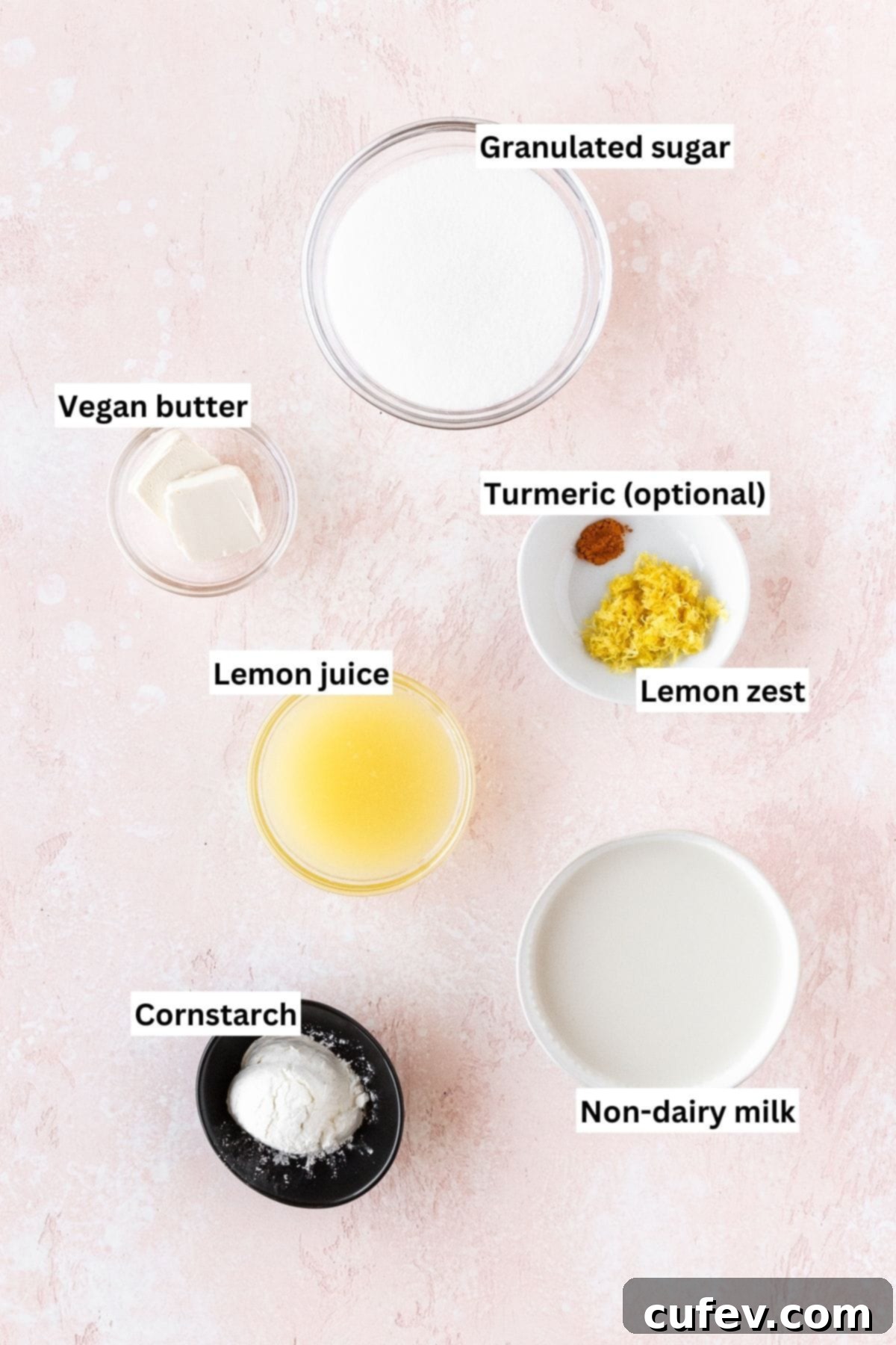 Velvety Vegan Lemon Curd 5 Ingredients needed for making vegan lemon curd measured out into bowls on a pink table with text overlay, including fresh lemons, vegan butter, sugar, cornstarch, and milk.