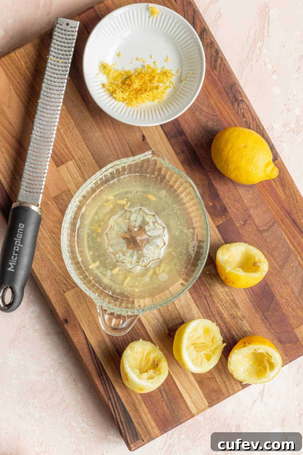 Velvety Vegan Lemon Curd 6 overhead shot of an old fashioned manual lemon juicer bowl filled with juice, a microplane, a plate of lemon zest, and several spent lemons on a wooden cutting board, showing the preparation of fresh lemons.