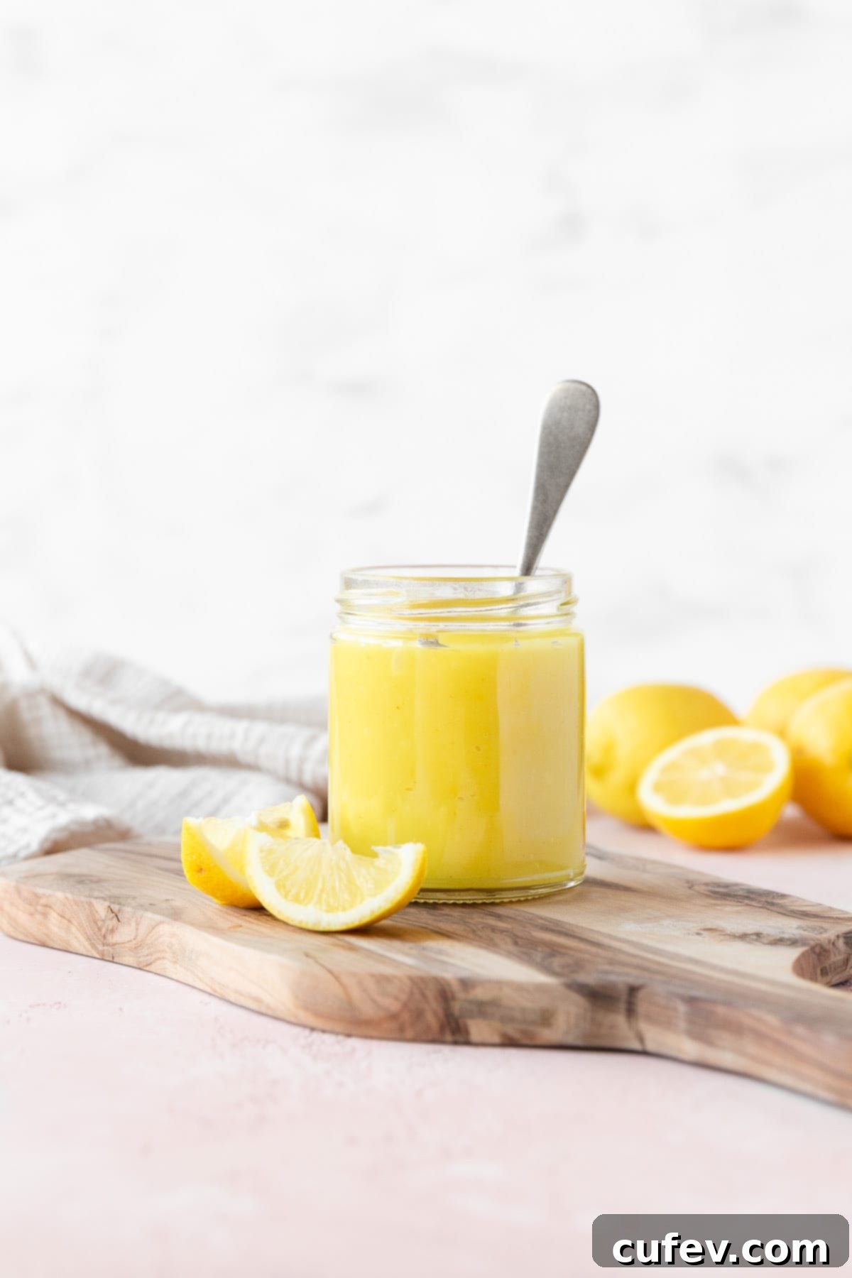 Velvety Vegan Lemon Curd 10 Side on shot of a small mason jar of vegan lemon curd with a silver spoon in it on a wooden cutting board with a few wedges of fresh lemon, ready to be enjoyed.