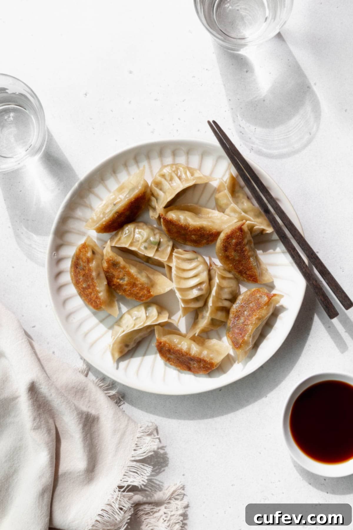 Overhead shot of vegetable gyoza on a white plate with wooden chopsticks.