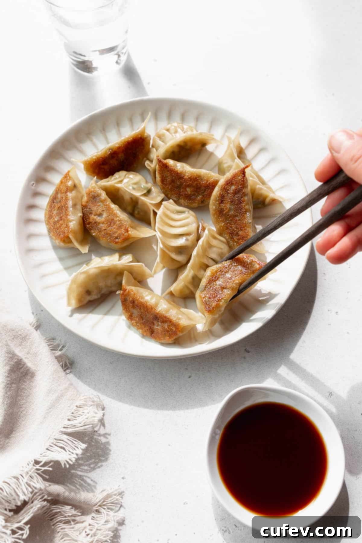 A hand holding chopsticks reaching to pick up a vegan gyoza off a plate. 
