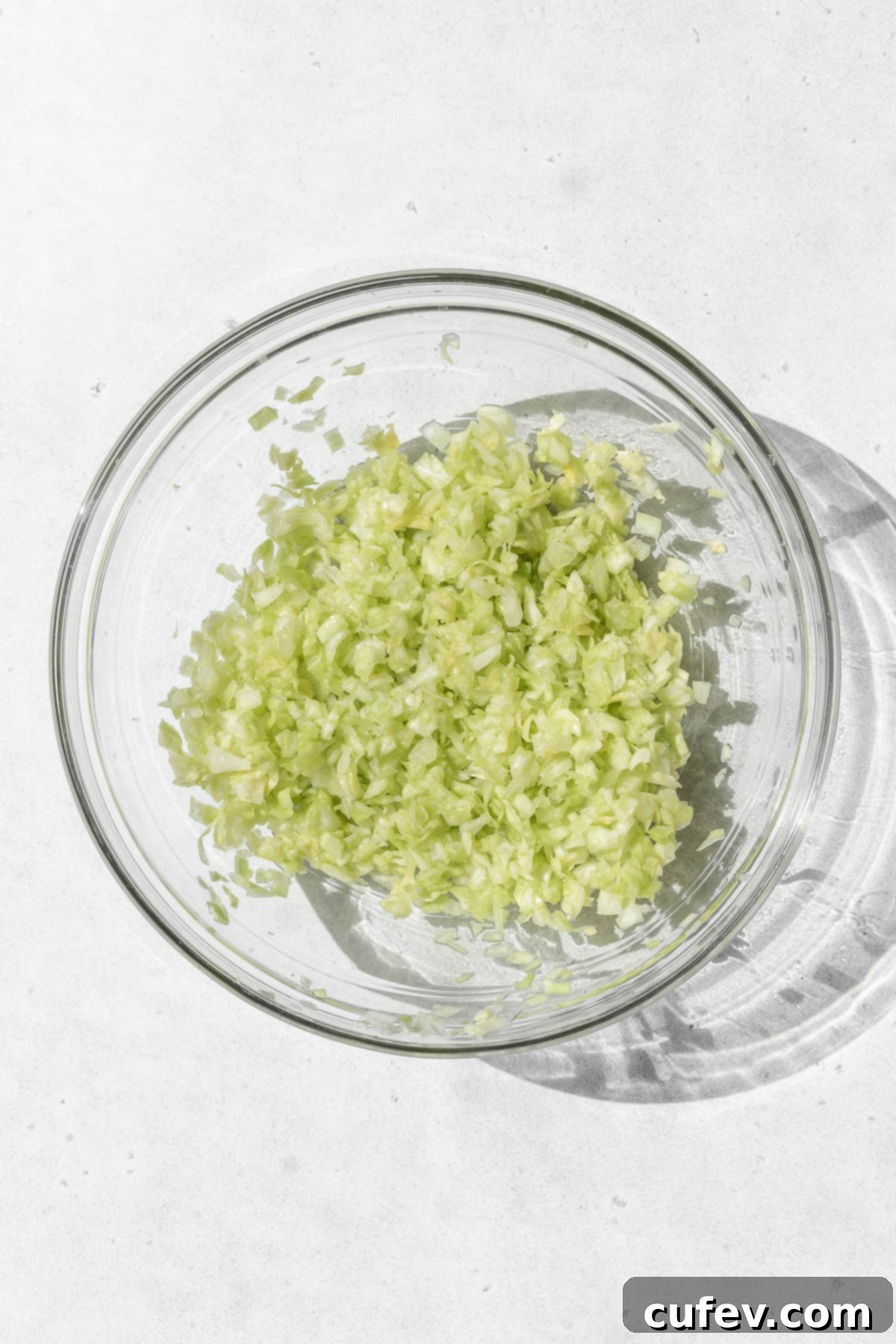 Minced cabbage in a glass bowl on a white surface, demonstrating the initial step of salting.