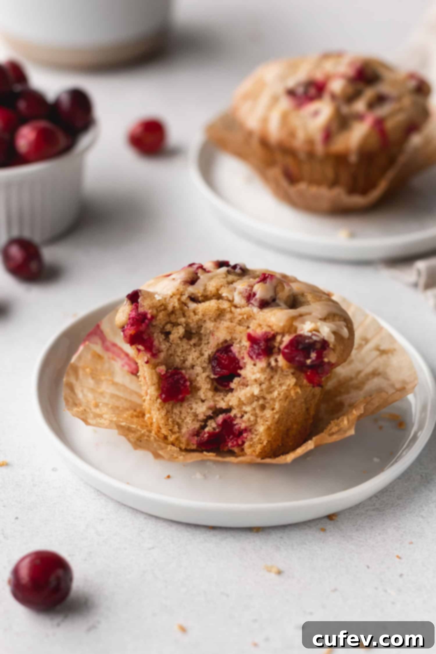 A cranberry orange muffin on a plate with a section bitten off, revealing its moist interior and visible cranberries.