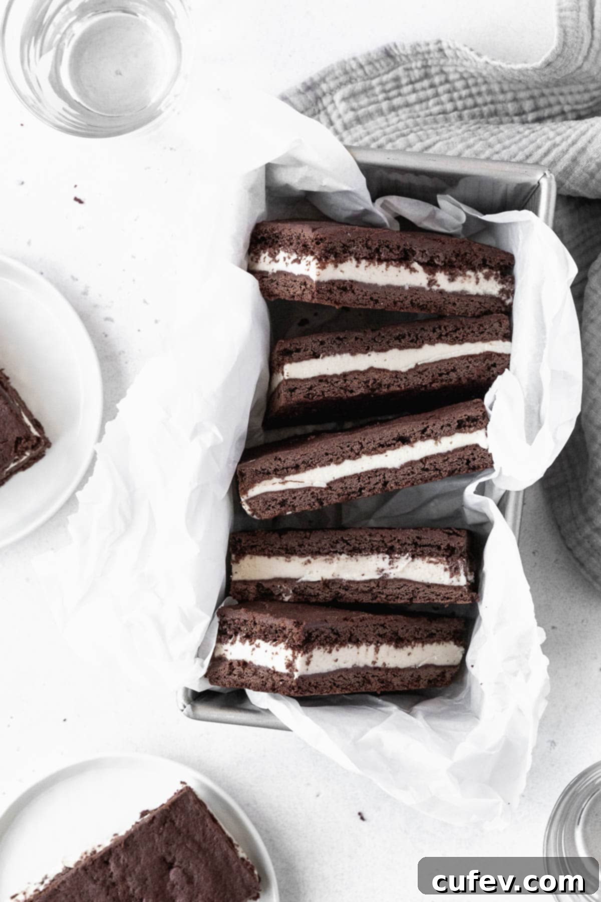 A collection of perfectly formed ice cream sandwich cookies, snugly arranged in a parchment paper-lined loaf pan, ready for the freezer.