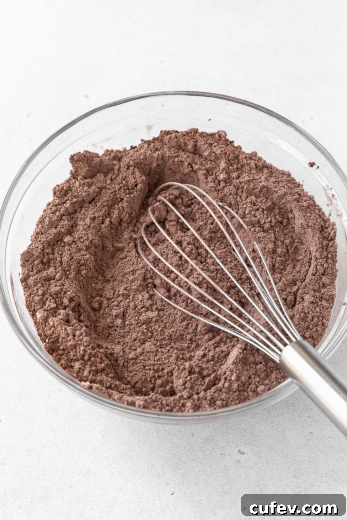 A glass mixing bowl containing a well-combined mixture of gluten-free flour and cocoa powder, ready for the next step.