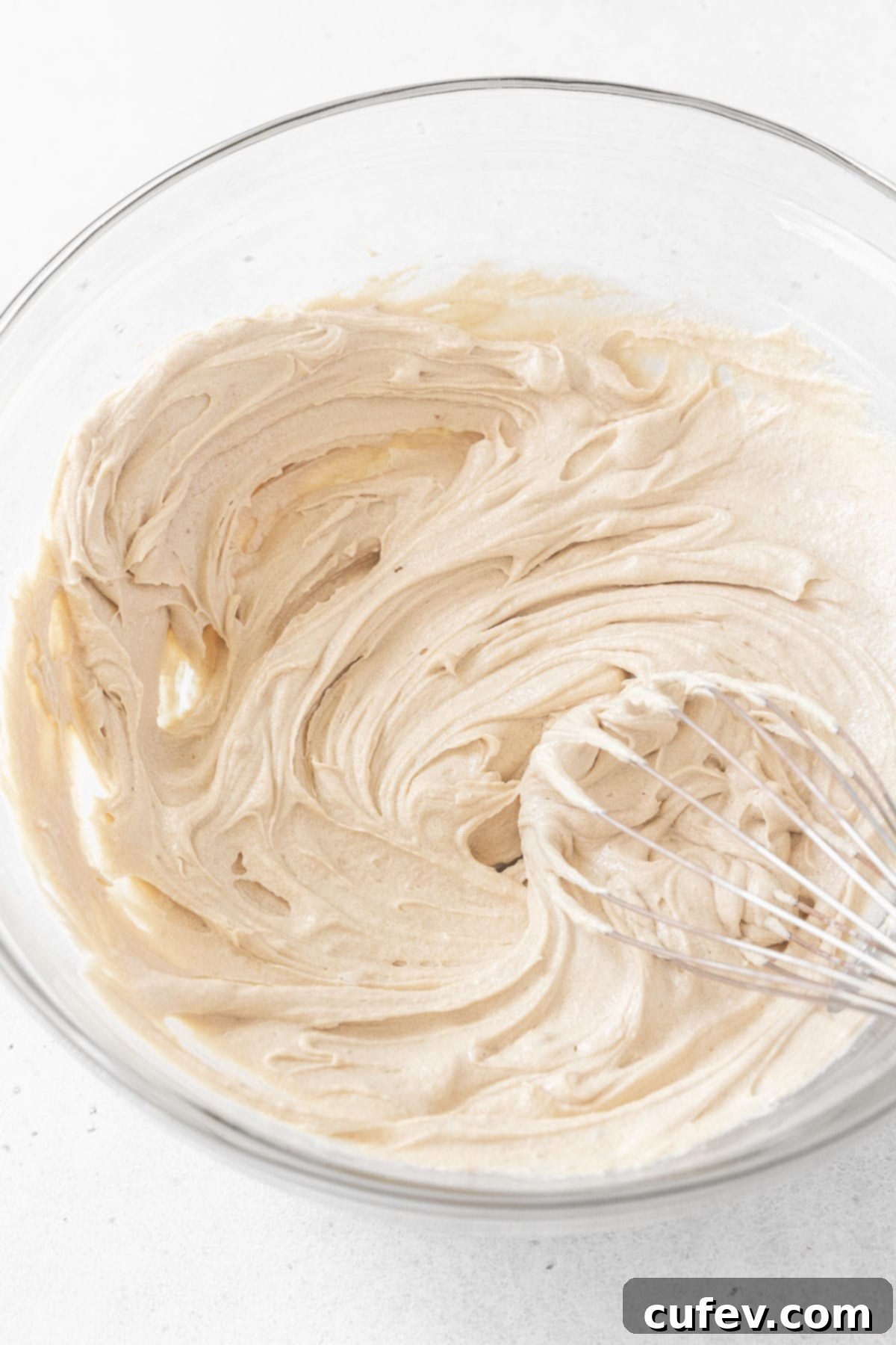 Vegan butter and light brown sugar expertly beaten together in a glass mixing bowl, showcasing a light and fluffy texture.