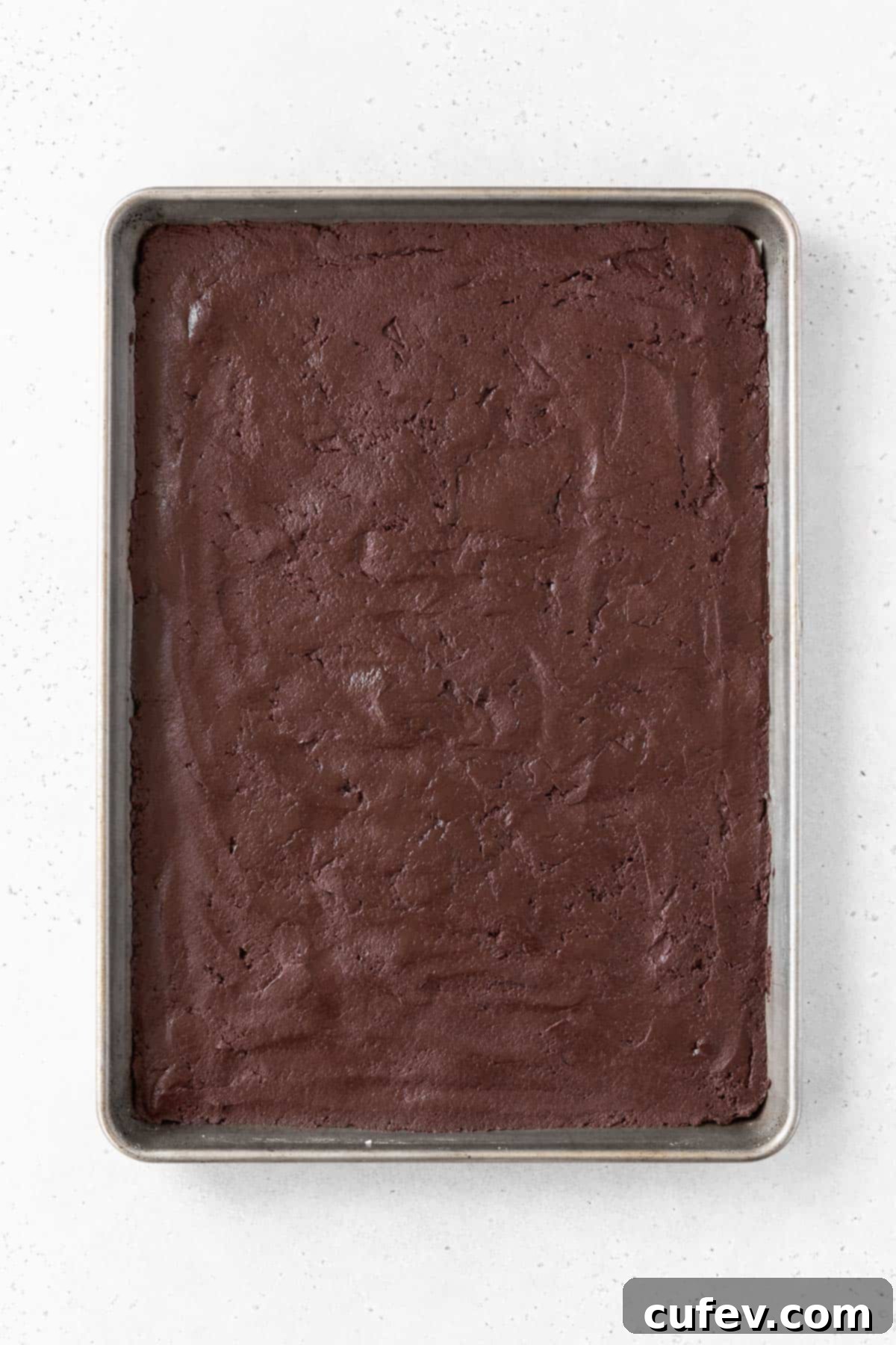 Smooth, dark chocolate sandwich cookie batter expertly spread across a baking sheet lined with parchment paper, ready for the oven.