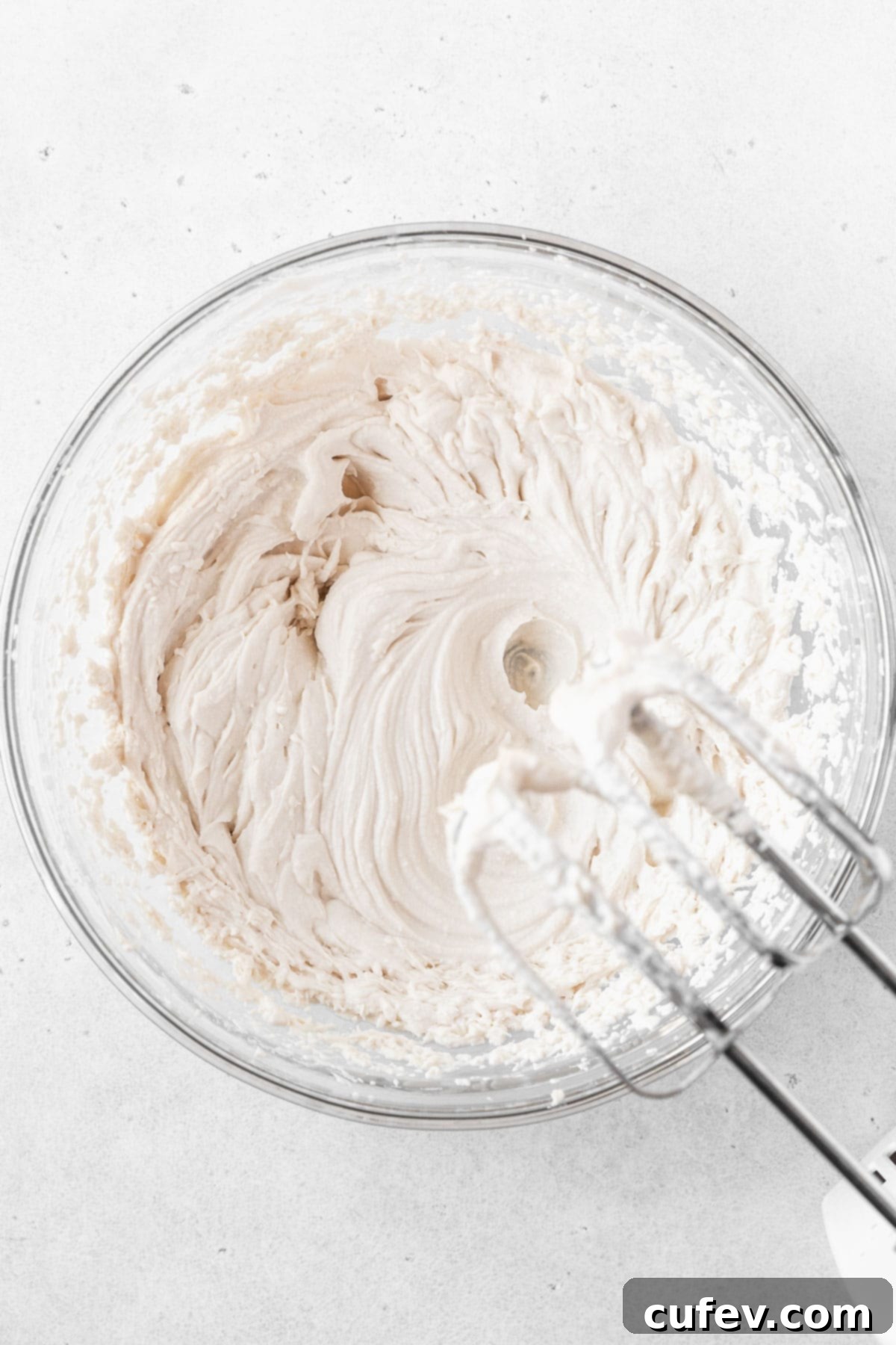 Oat milk whipping cream being vigorously beaten in a glass mixing bowl, creating a light and airy texture for the dairy-free ice cream.