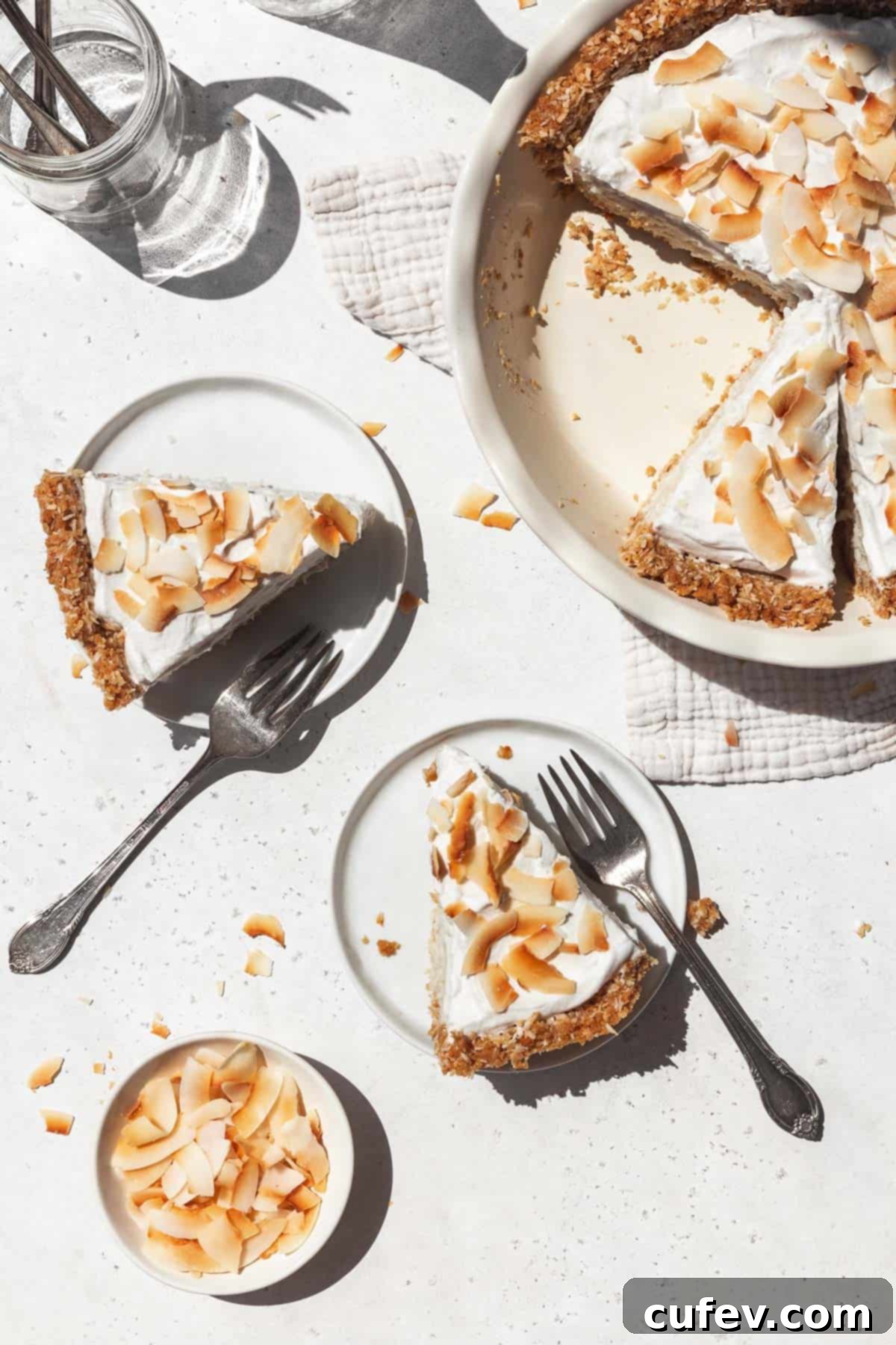 Overhead shot of two dessert plates each with a slice of creamy vegan coconut cream pie topped with toasted coconut flakes.