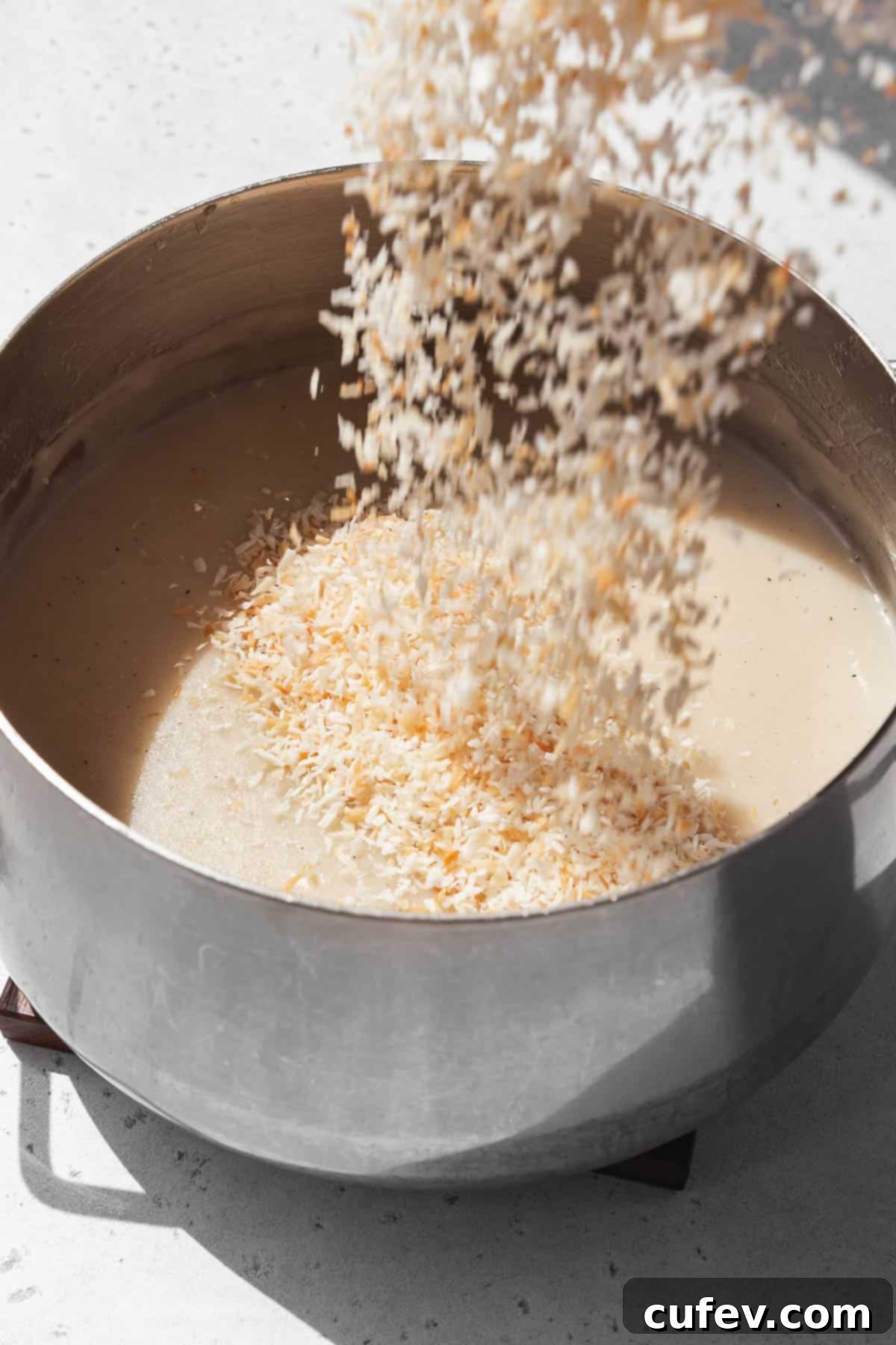 Action shot of toasted desiccated coconut being poured into the vegan custard base in the saucepan.