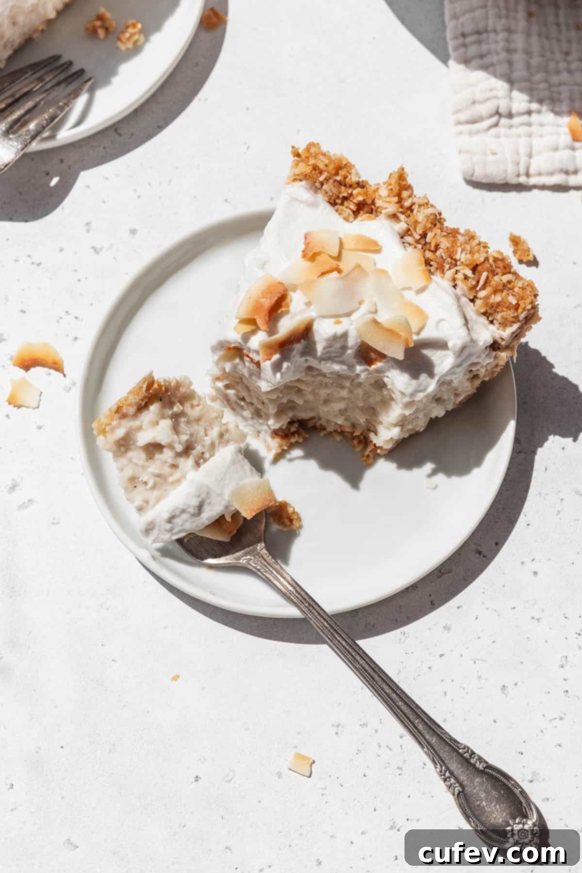 Small white dessert plate with a slice of GF no-bake plant-based coconut cream pie with a silver fork taking a bite out of it.
