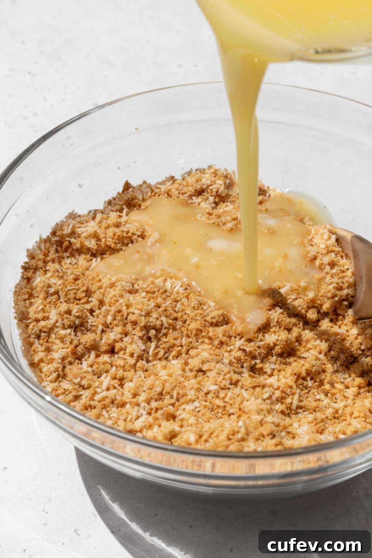 Action shot of melted vegan butter being poured into the bowl with the graham cracker crumb and toasted coconut mixture.