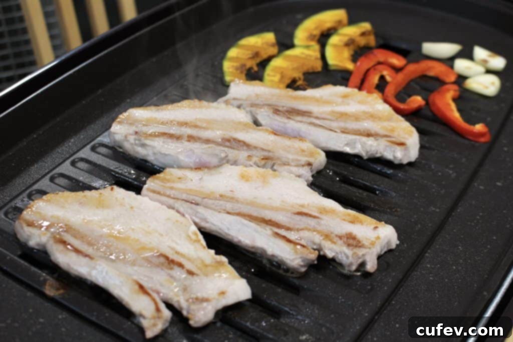 Pork belly and assorted vegetables sizzling on a hot tabletop grill