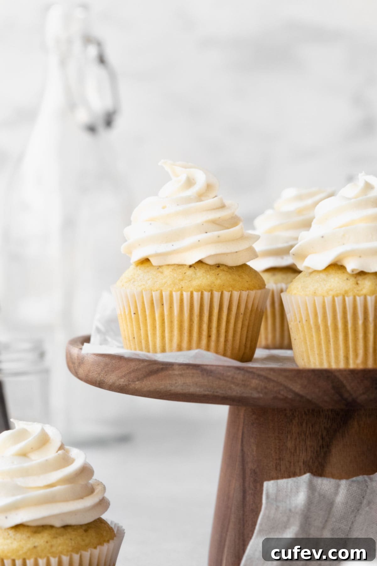 Side on shot of vanilla buttercream topped vegan cupcakes on a wooden cake platter.