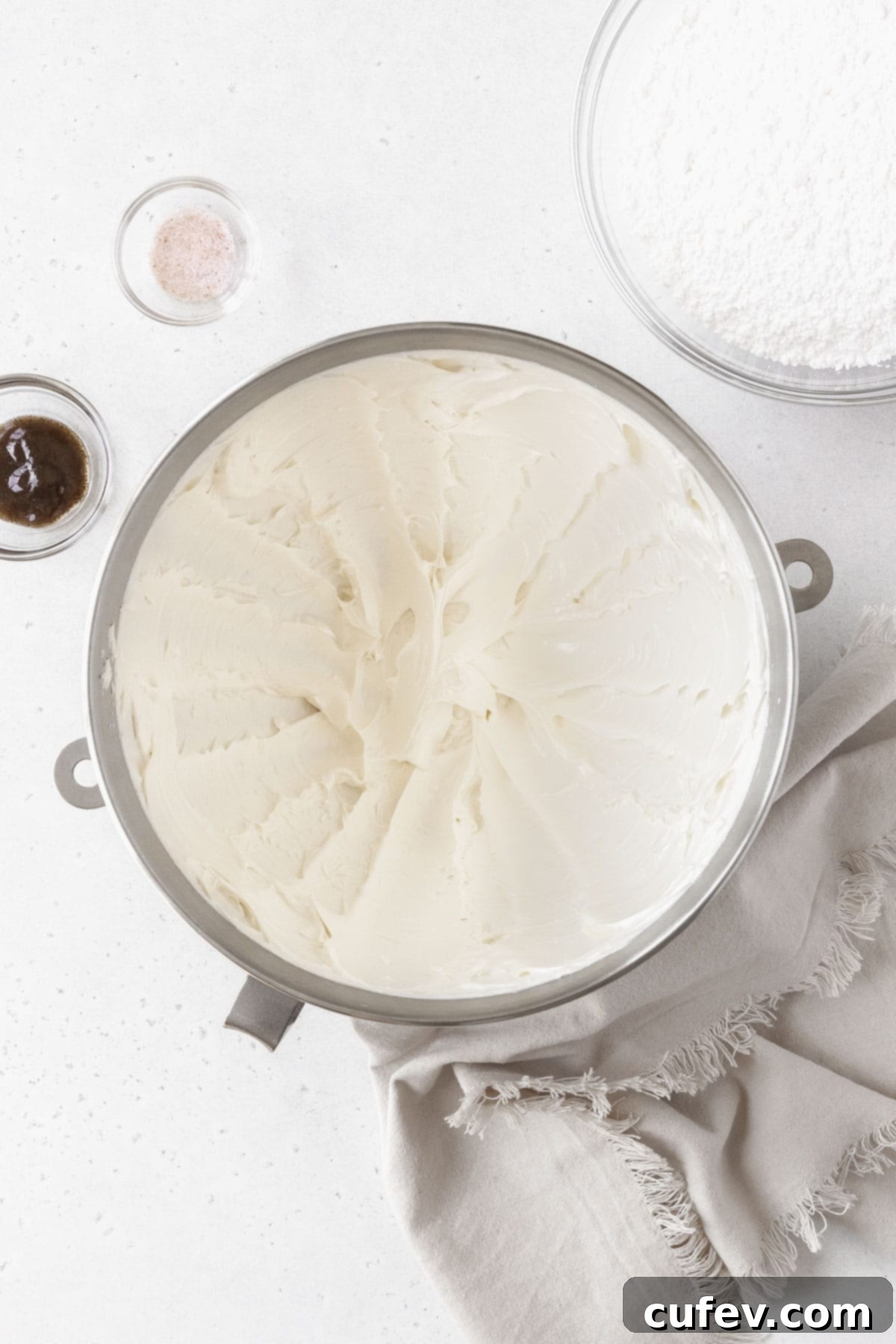 A silver mixing bowl of whipped butter next to a bowl of powdered sugar and vanilla.