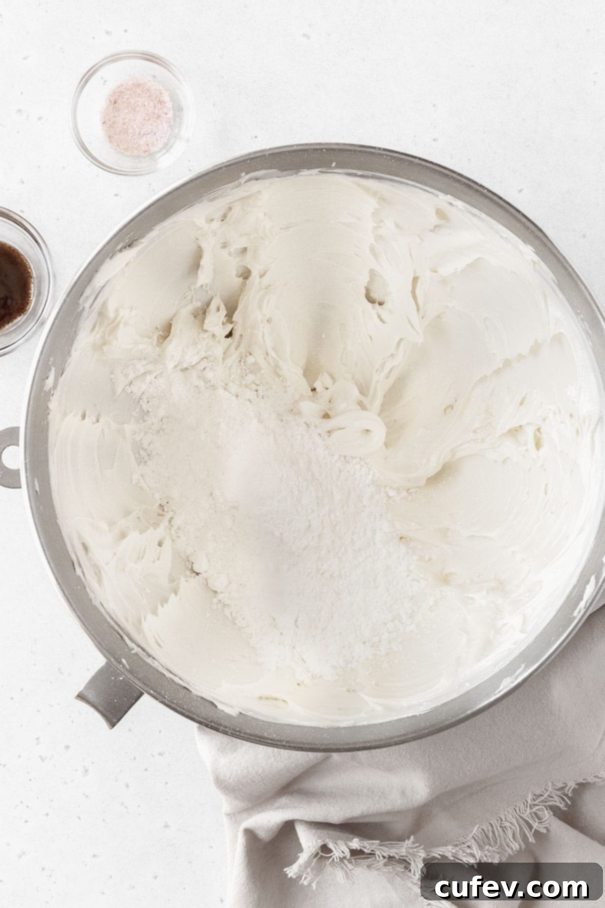 Powdered sugar being added to the large bowl of whipped butter.