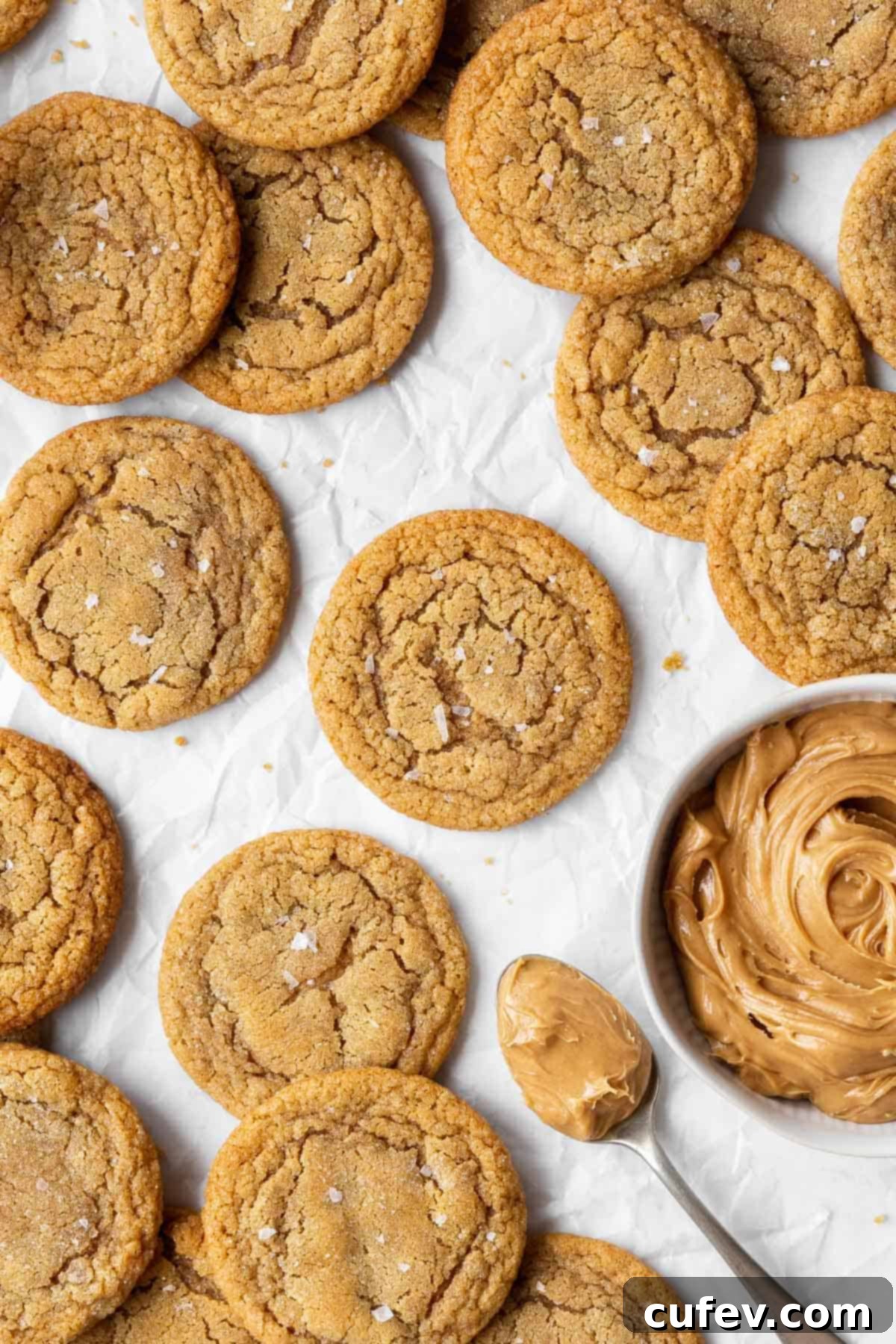Dairy-free peanut butter cookies arranged neatly on parchment paper, accompanied by a spoonful of creamy peanut butter and a bowl of the same, highlighting the key ingredient.