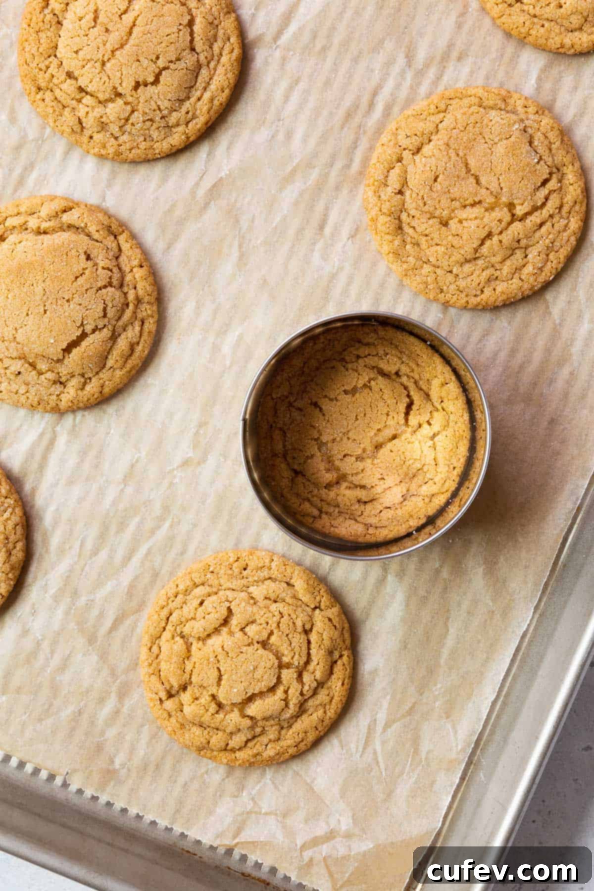Demonstrating how to shape the warm peanut butter cookie with a round cookie cutter on a parchment paper-lined baking sheet for a perfectly circular finish.