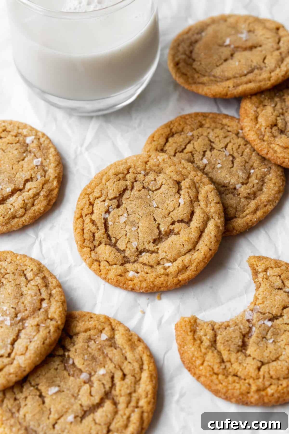 An up-close shot of the freshly baked dairy-free peanut butter cookies on parchment paper. One of the cookies has a bite taken out of it, revealing its soft and chewy interior texture.