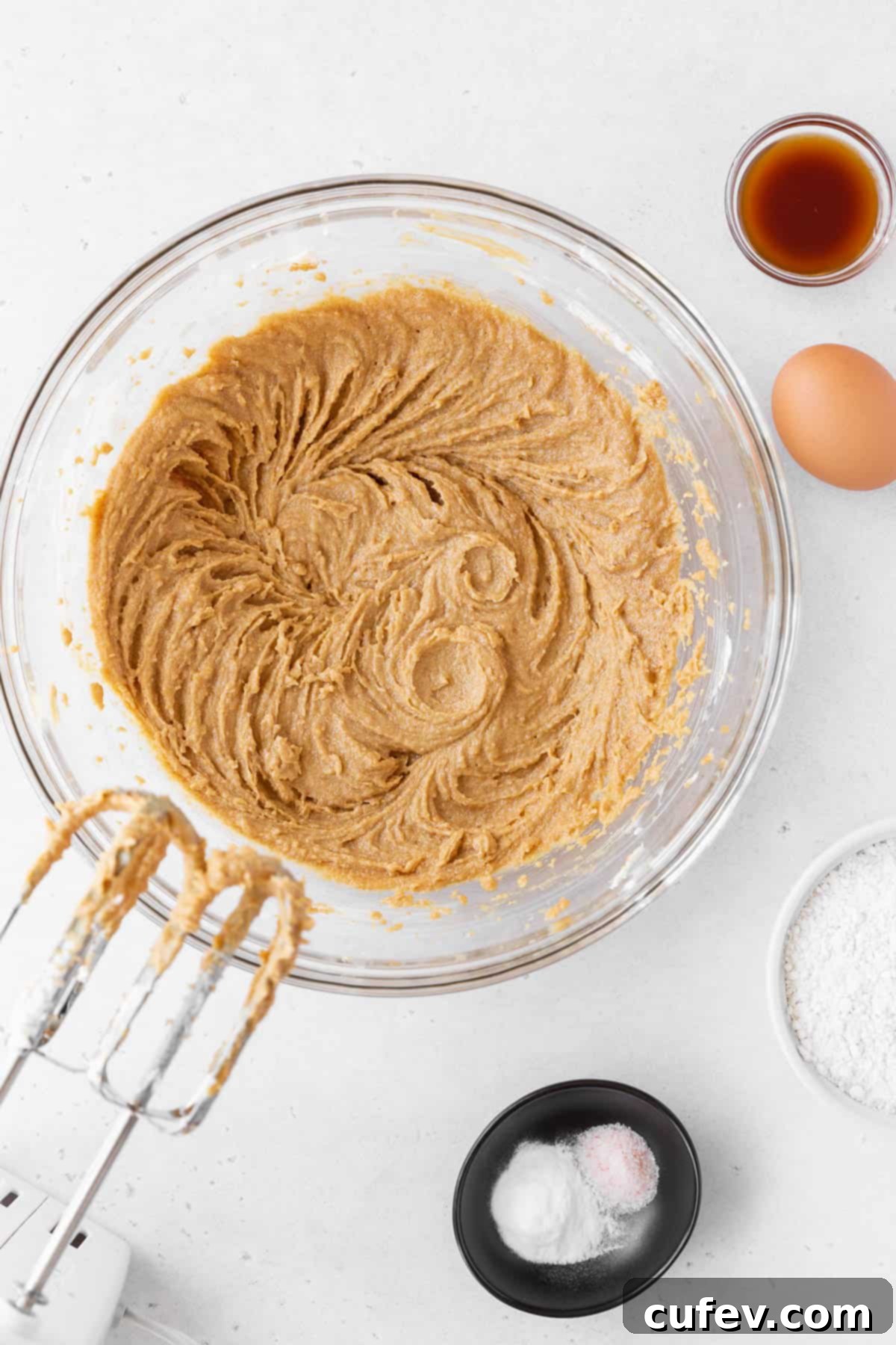 Blending the peanut butter and vegan butter together in a glass mixing bowl until light and fluffy, showing the creaming process.