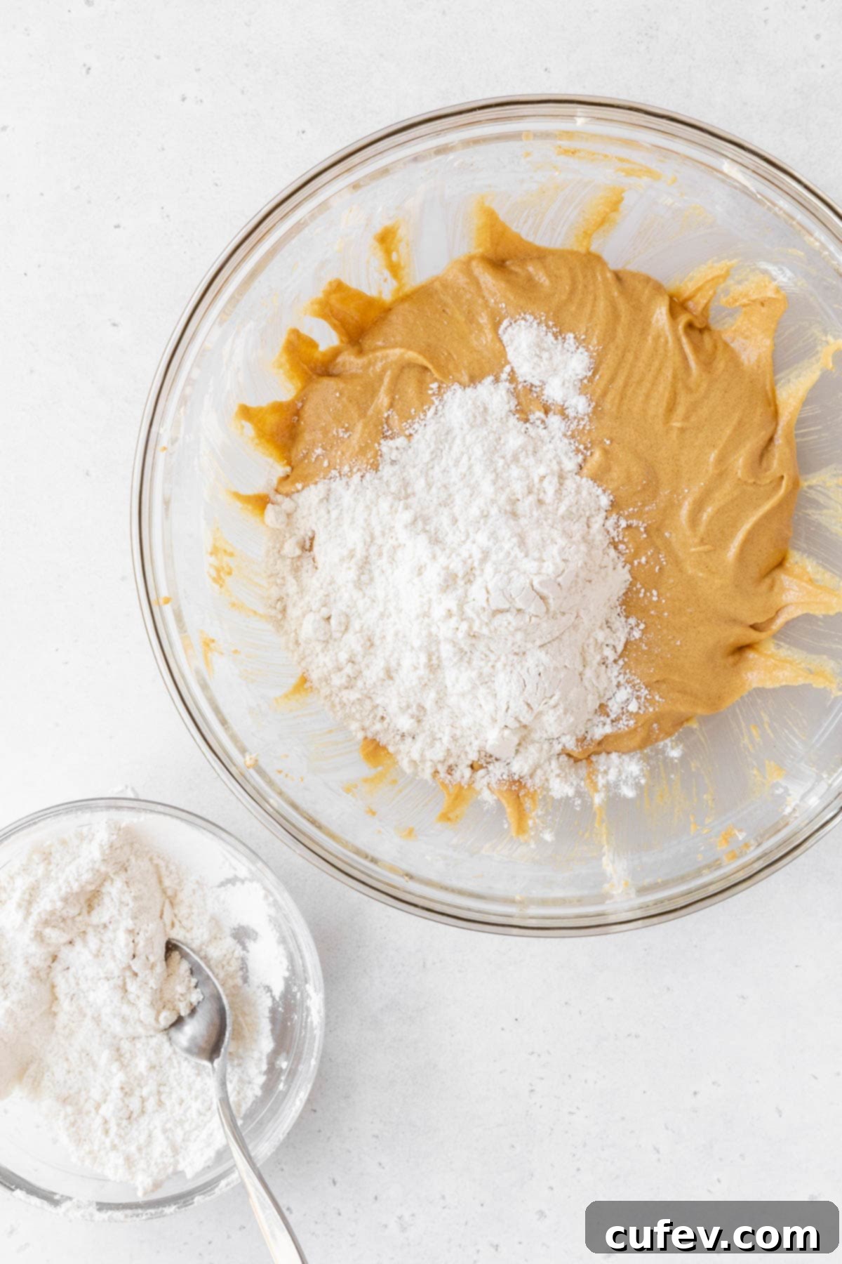 Adding the thoroughly mixed flour mixture to the peanut butter and wet ingredient mixture in the mixing bowl, gently combining.