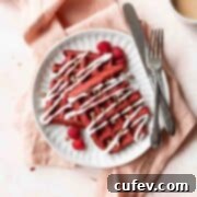 A square shot of a white plate of red velvet waffles with cream cheese drizzle and pecans.